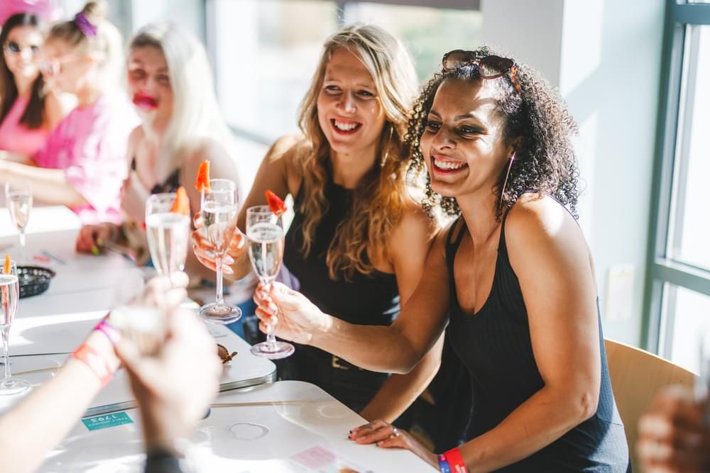 Two women happily toasting their glasses on a Big Weekender Bottomless Brunch.