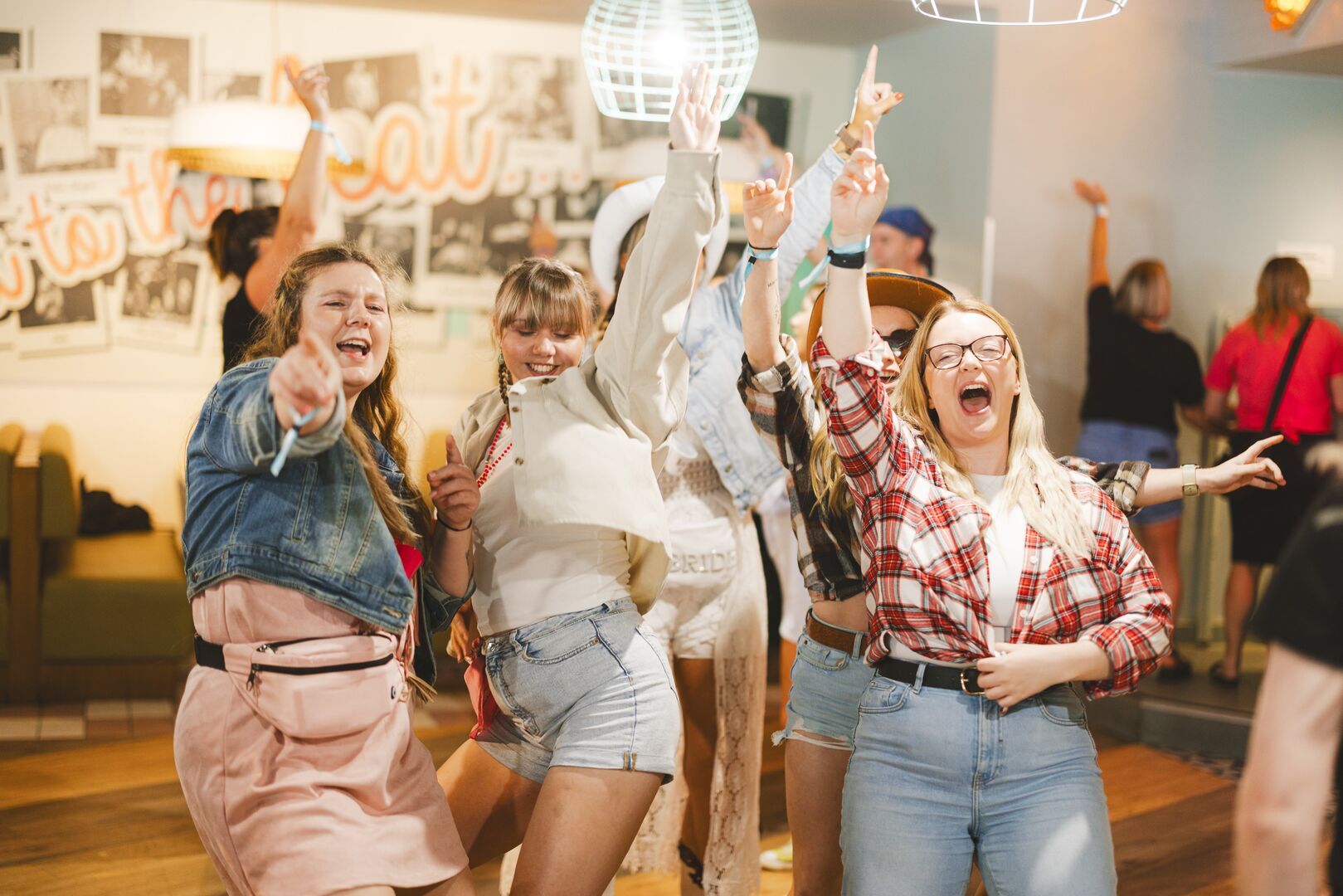 A group of friends sing together at Bottomless Brunch, with their hands in the air while they dance.