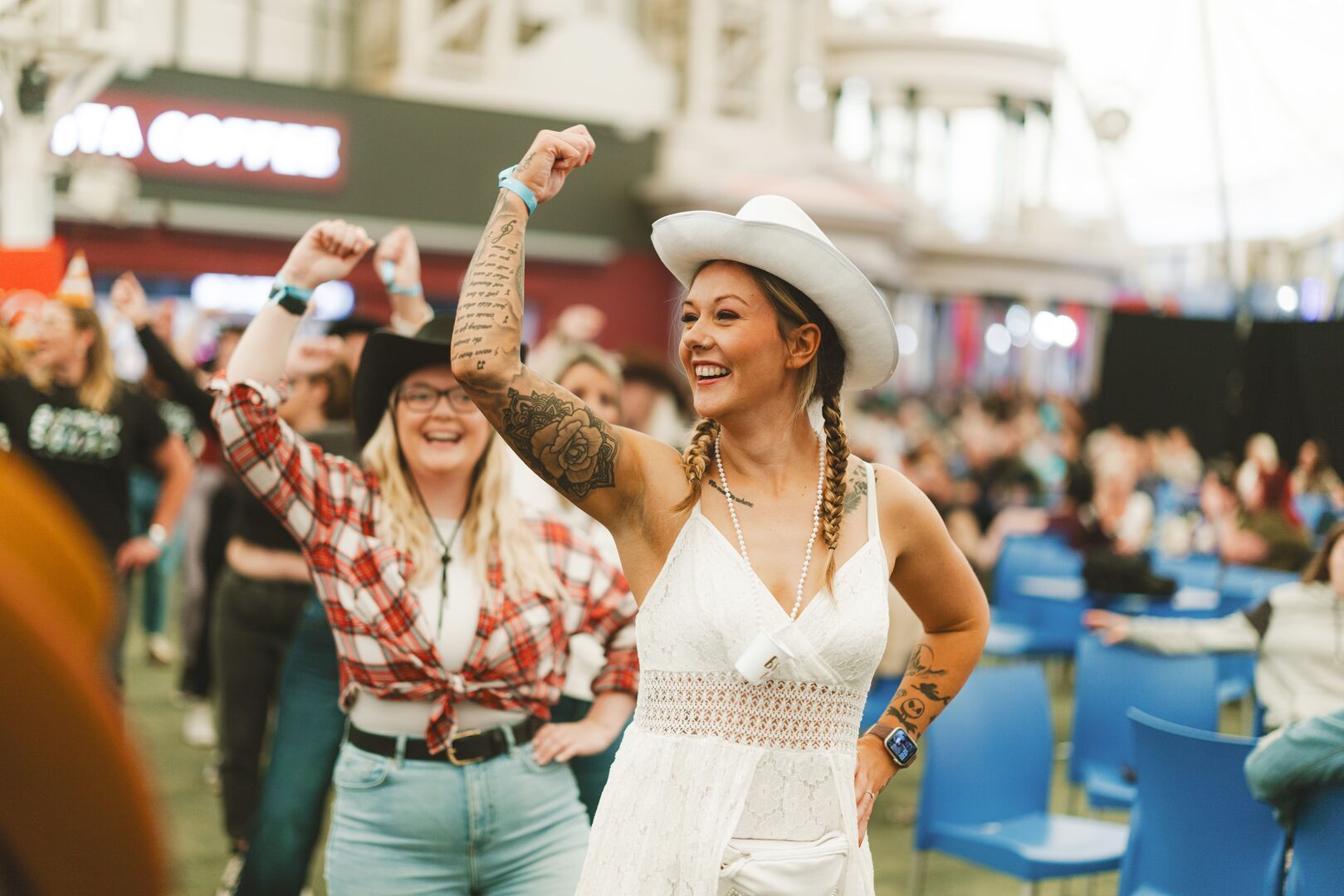 A young woman dancing in the crowd during the Saddle Up activity at Minehead resort, she is wearing a white cowboy hat and a white dress and a necklace that says 'bride to be'.