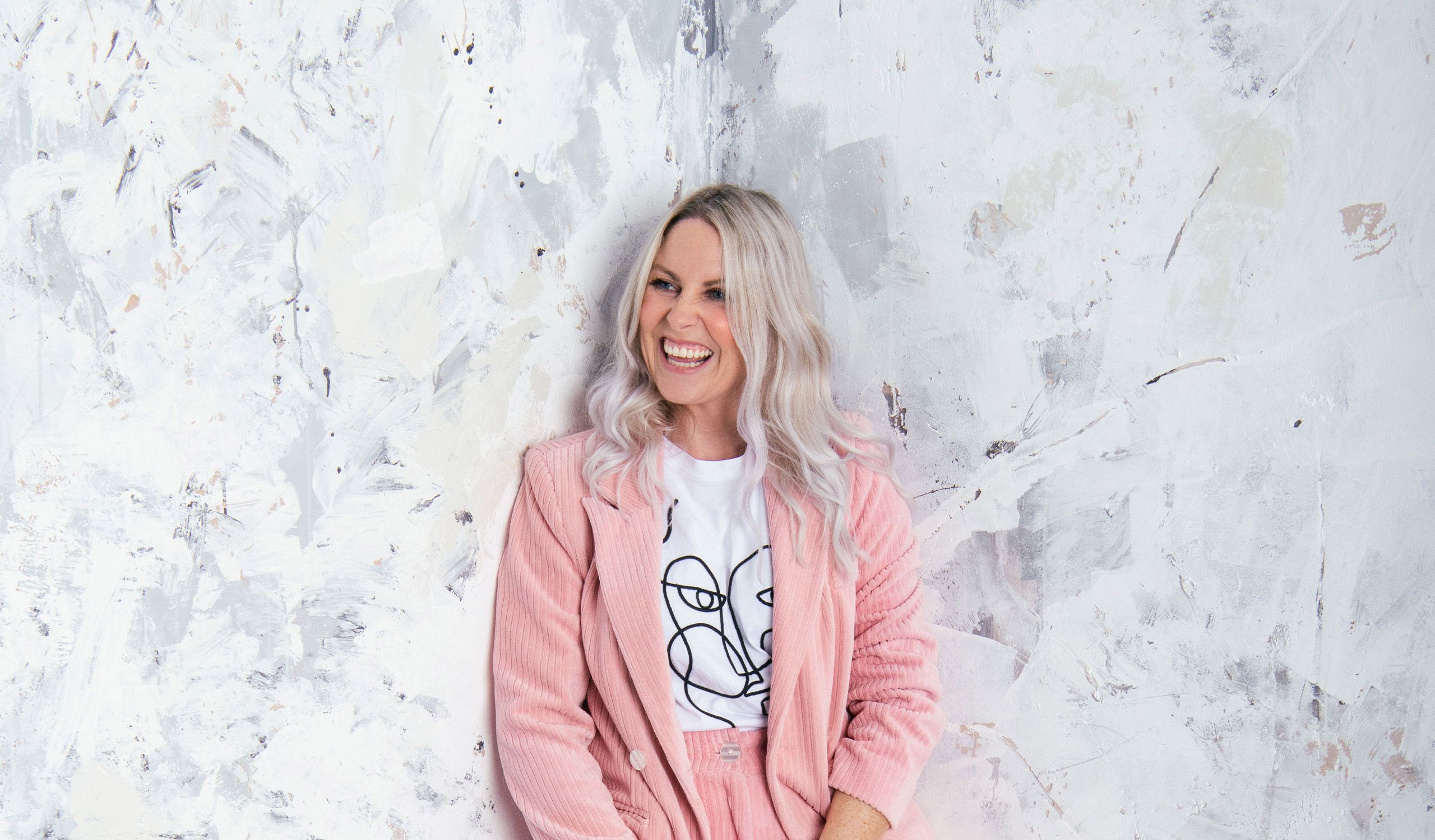 Charlie Hedges laughing in a pink suit against a marble white background.