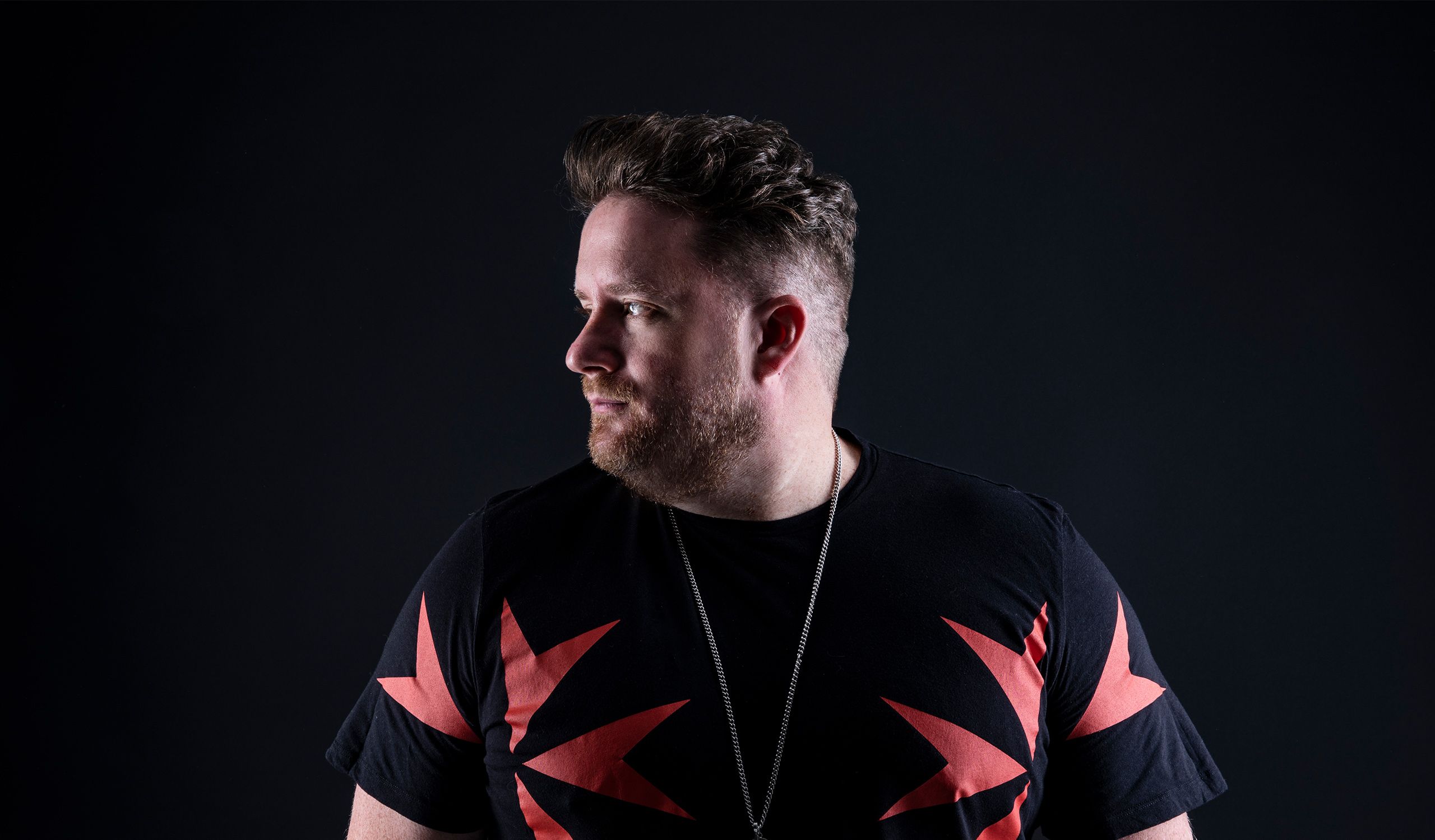 Eats Everything looking over his right shoulder. He is wearing a necklace and a black and red t-shirt.