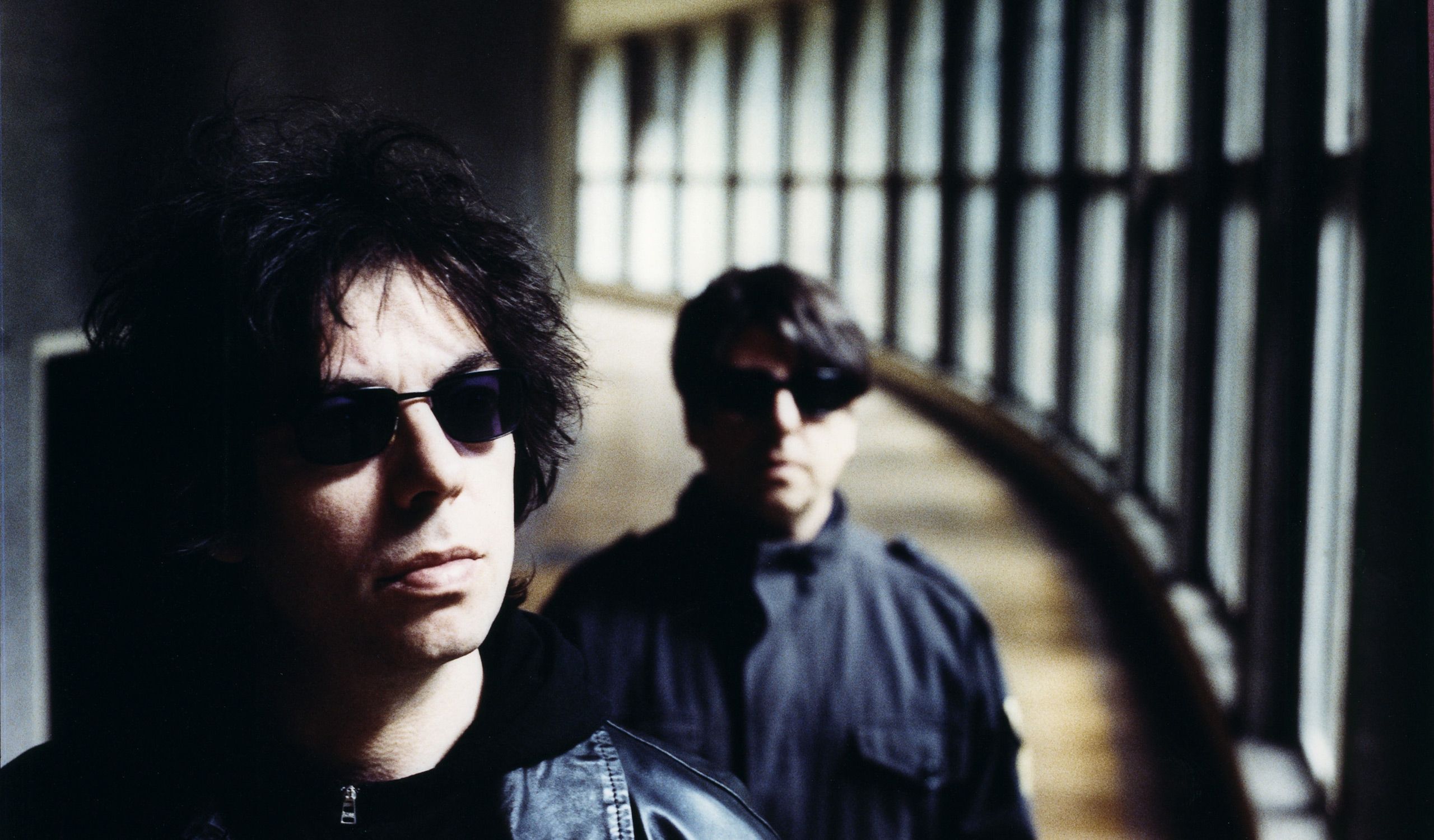 Members of the band Echo & the Bunnymen wearing sunglasses and all black in a tunnel.