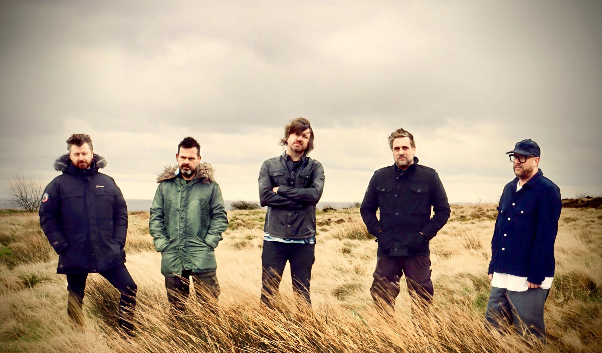 The 5 members of Embrace standing, in a row, in a field.