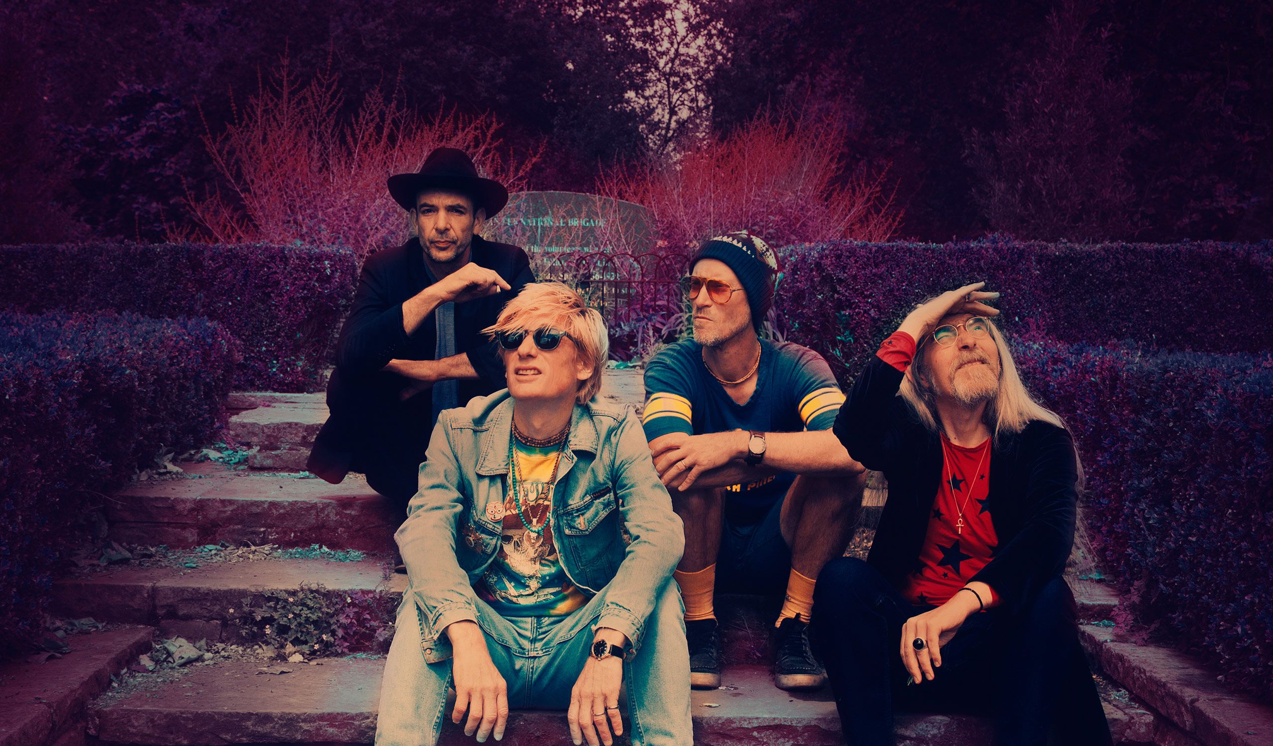 The 4 members of Kula Shaker sitting on steps in a garden.