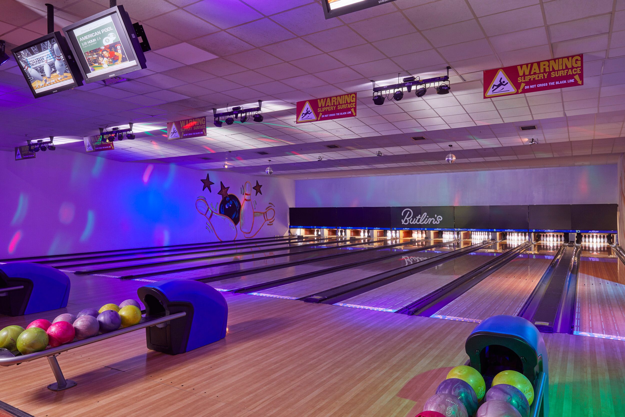 An empty bowling alley with bowling pins and balls.