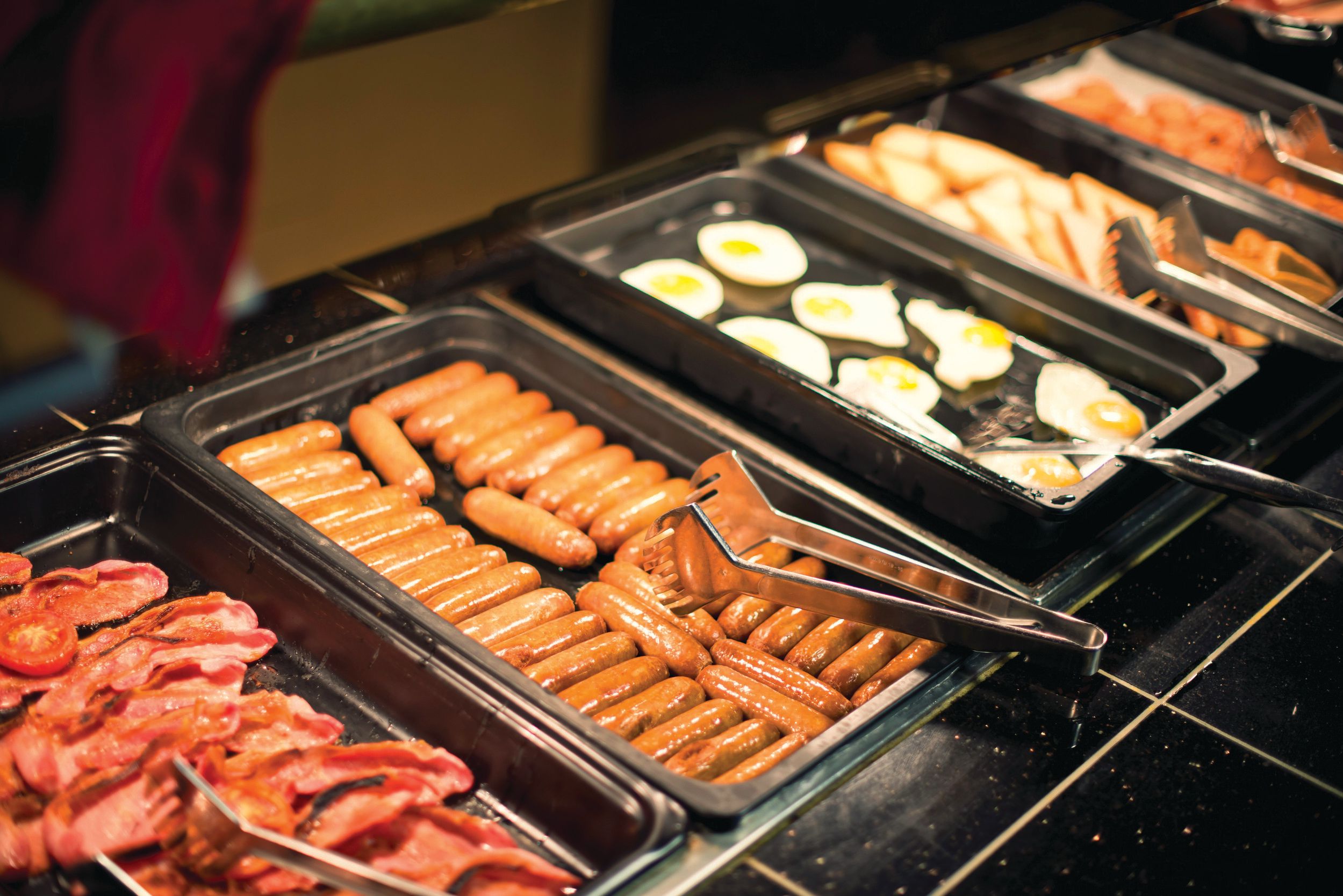 A set of food trays filled with sausages, egg, bacons and toasts.