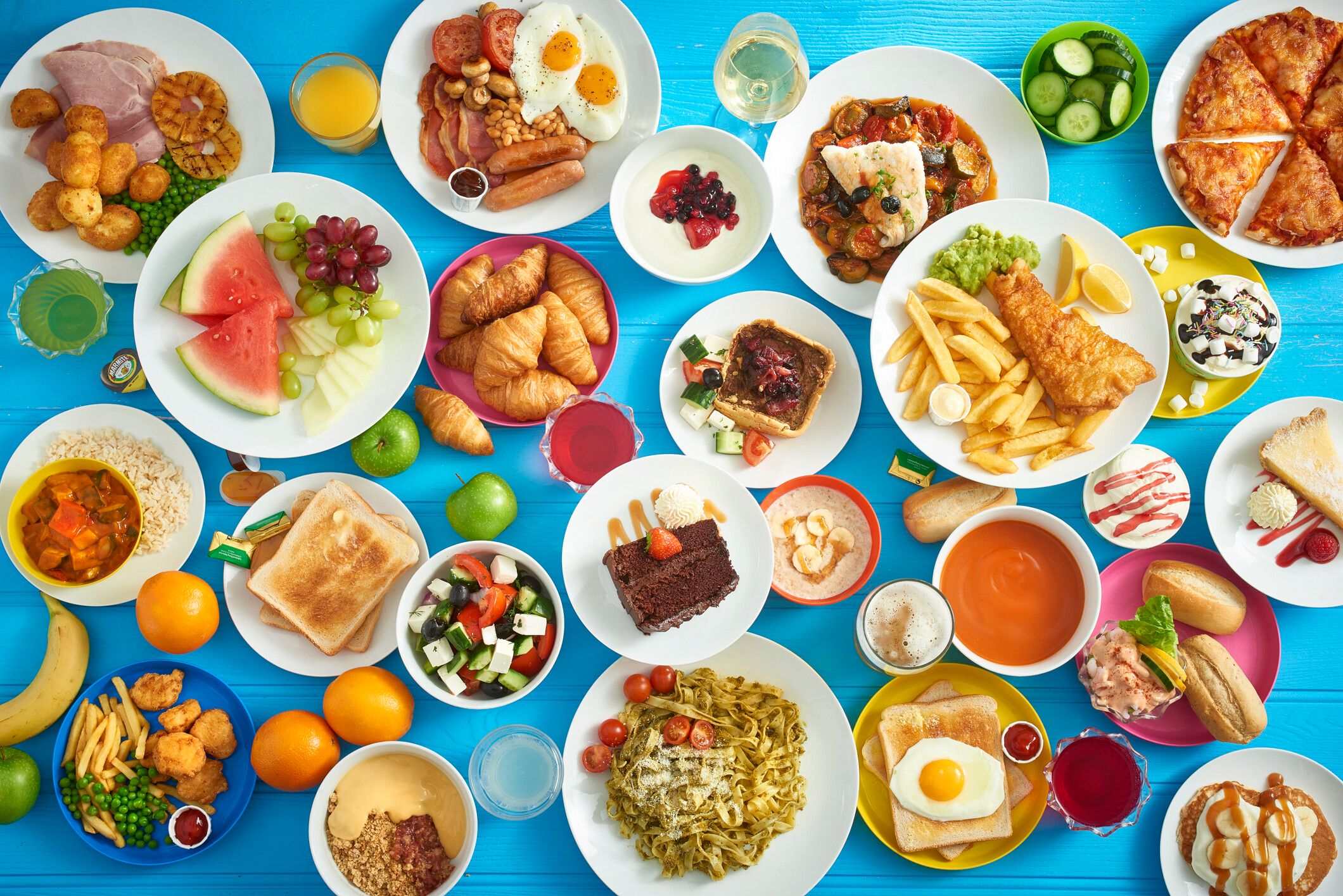 A table filled with different types of food such as fish & chips, desserts, pasta and English breakfast.