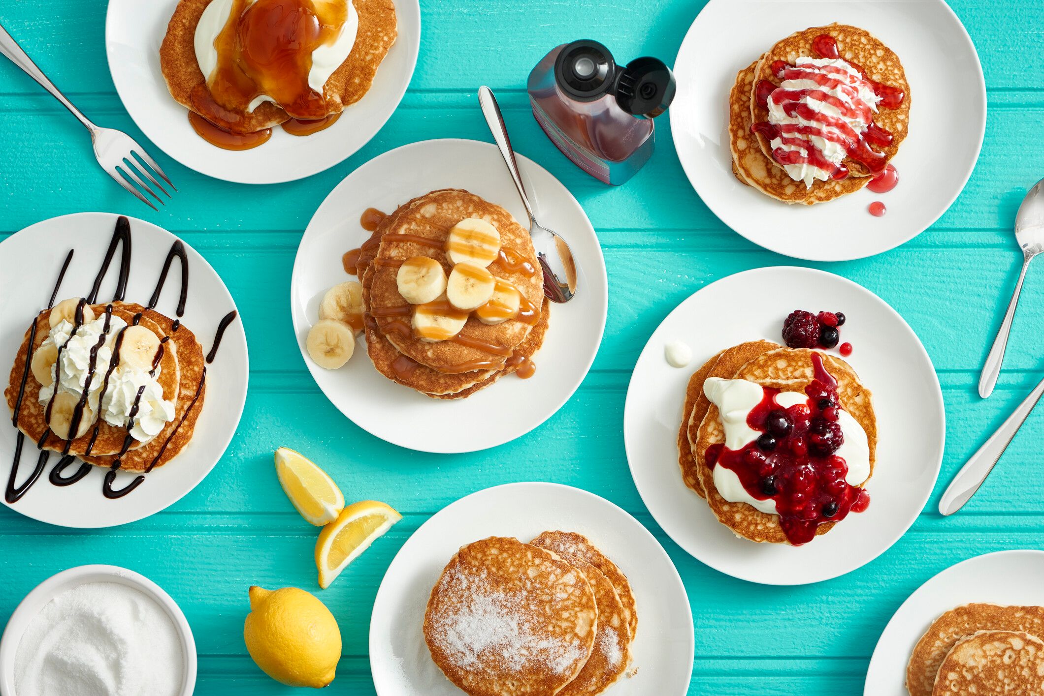 A table full of pancakes with different toppings such as bananas, creams and berries.
