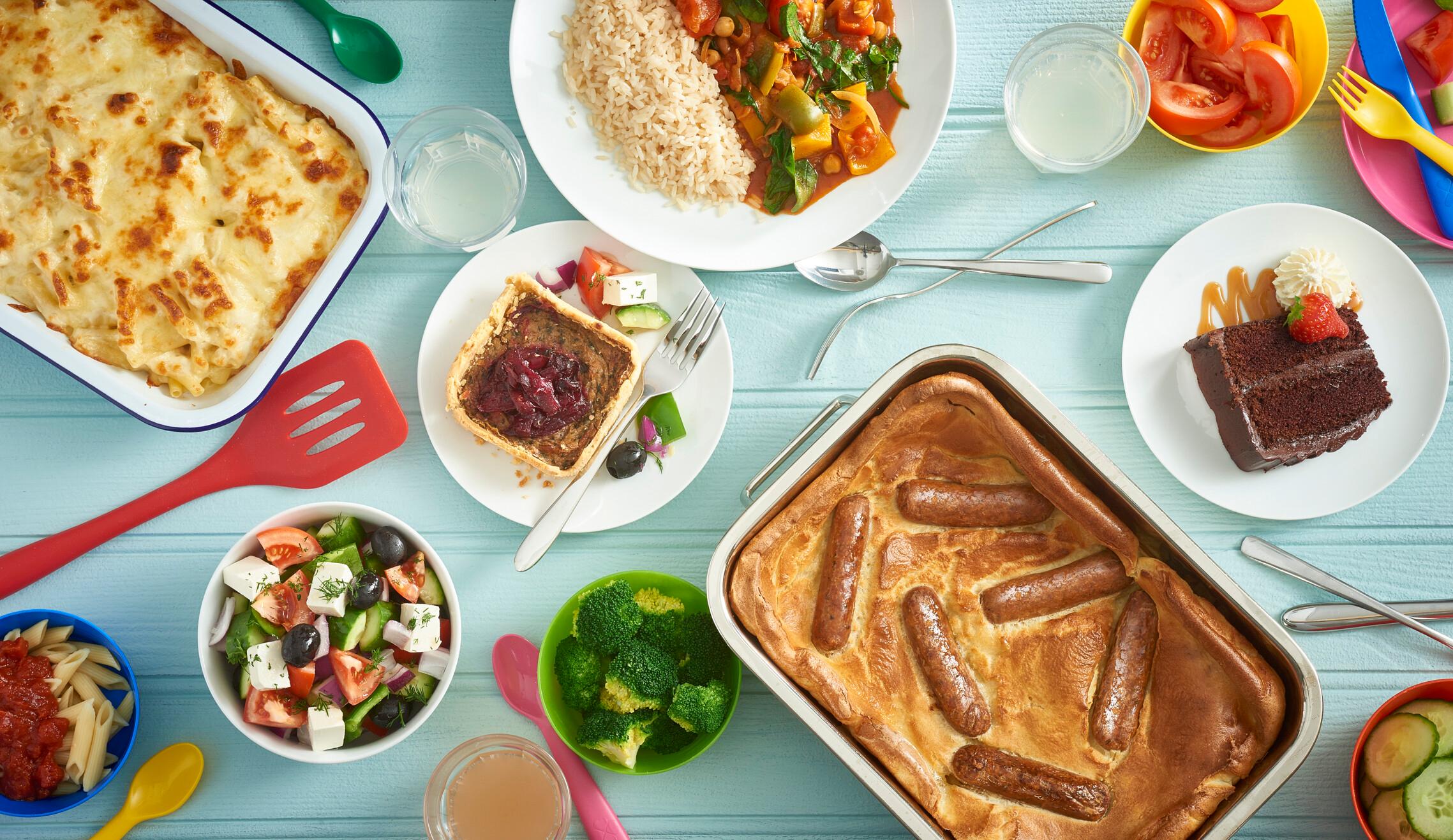 A table filled with food such as sausages, macaroni, salad and cake.