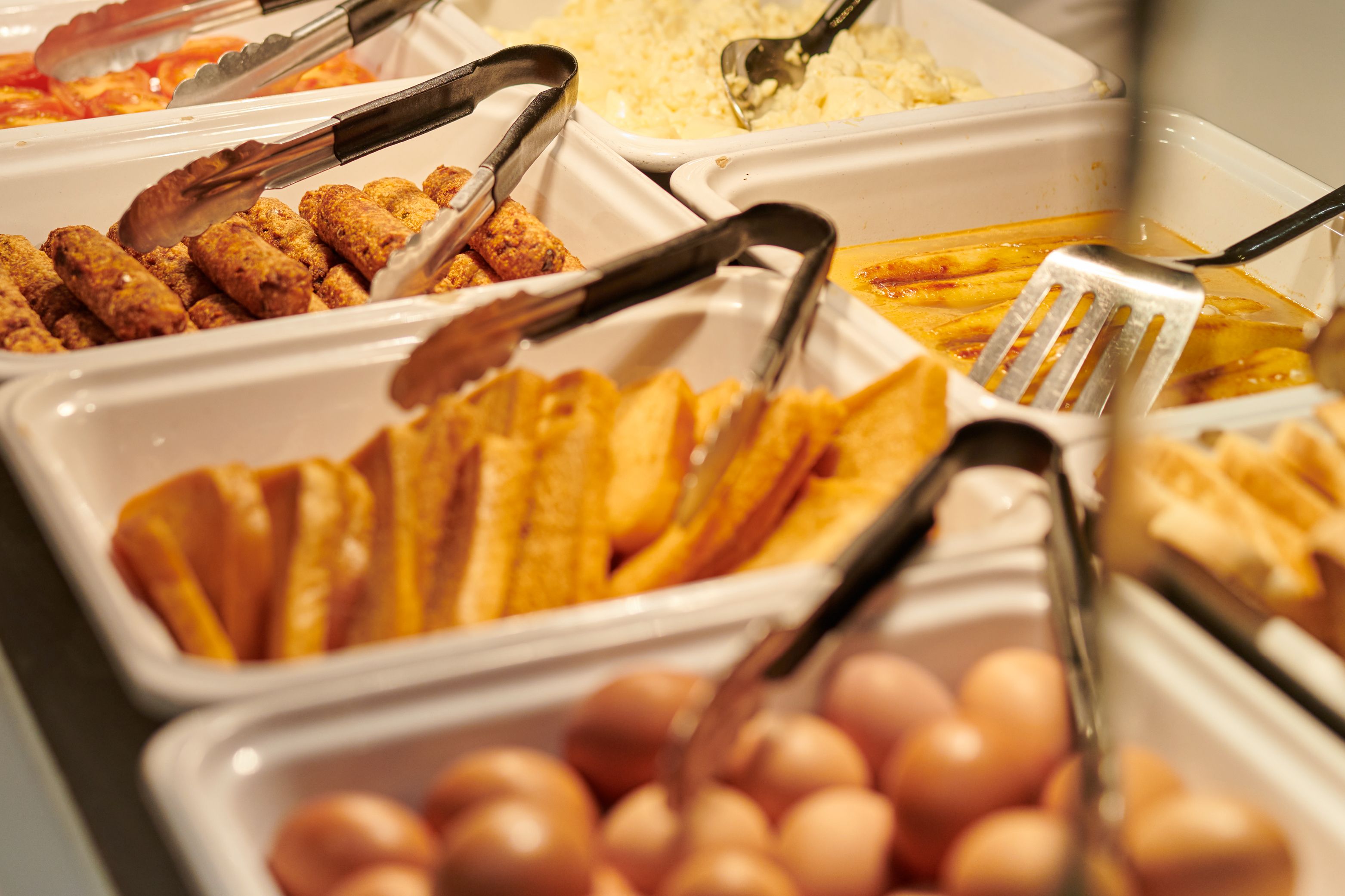 A table filled with foods including eggs, toasts, sausages, rice and tomatoes.