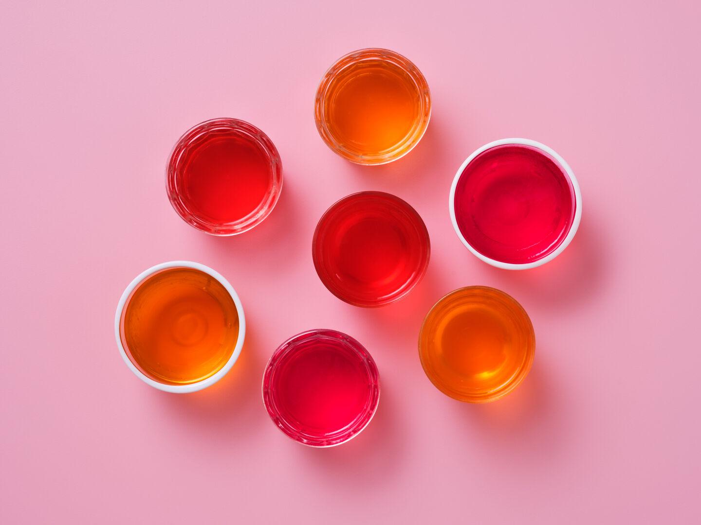Pots of red and orange jelly on a pink background.