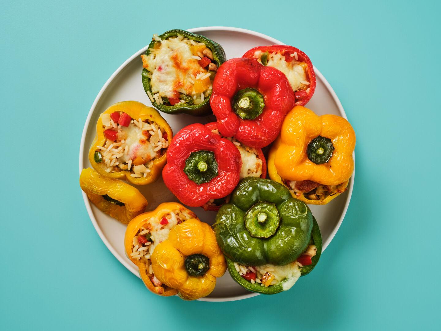 A plate of red, yellow and green peppers stuffed with rice and cheese, on a teal background.