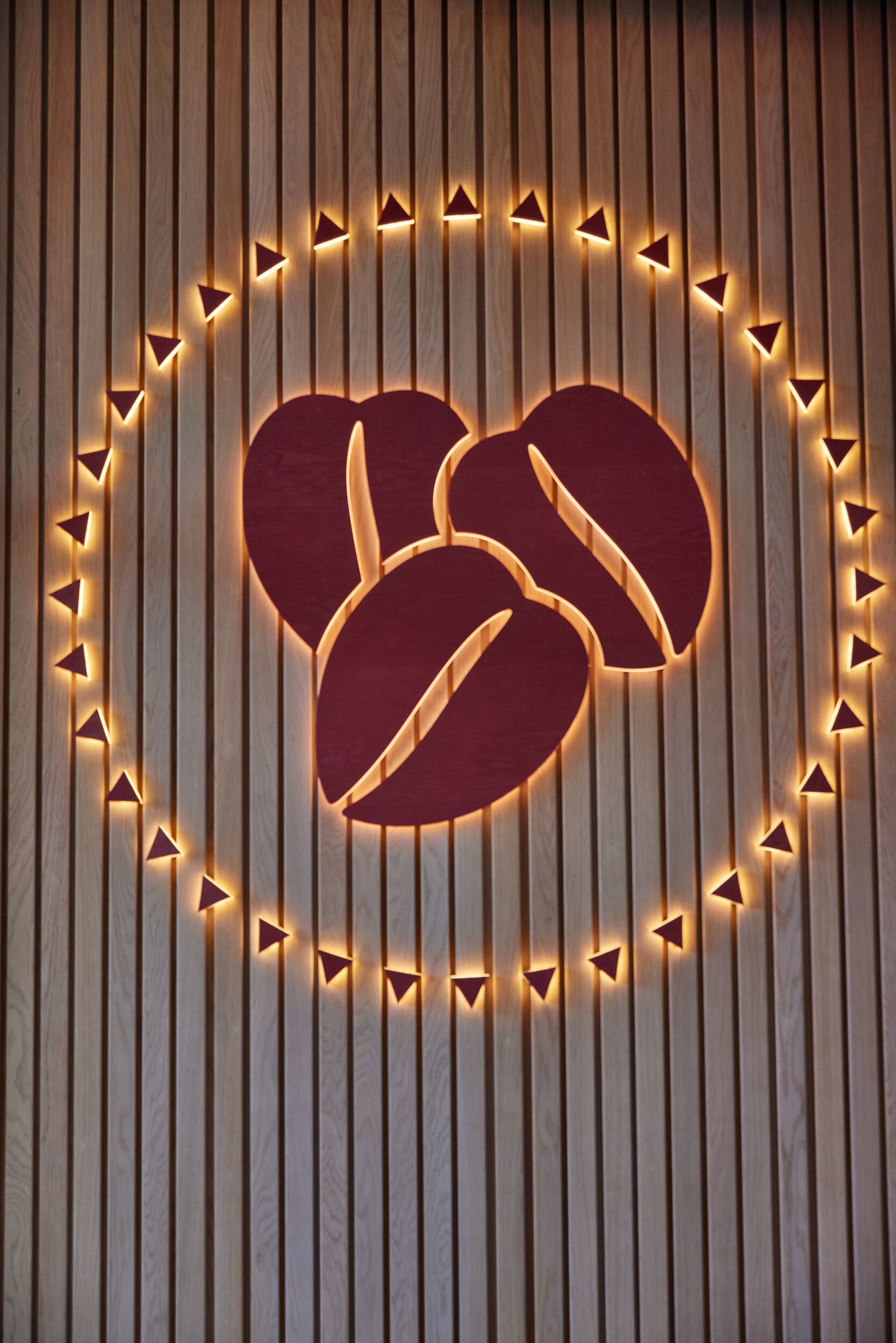 A close-up image of the Costa Coffee logo. Three coffee beans sit together in a circle, are are lit up. The logo is placed on a wood-paneled wall.