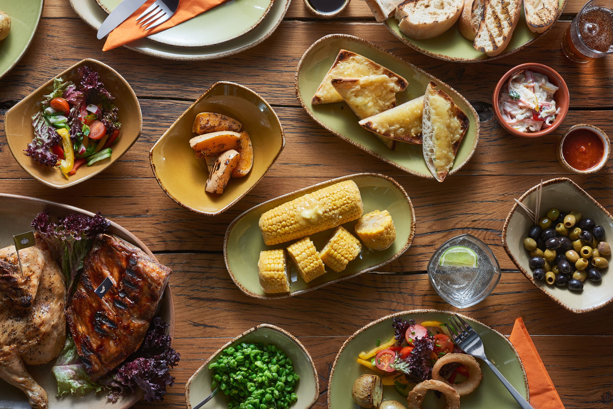 A table full of different types of food such as grilled chicken, corn, salad and toasts.