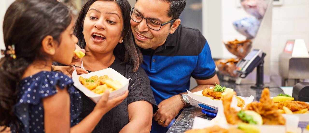 A mother feeding her daughter with chicken.