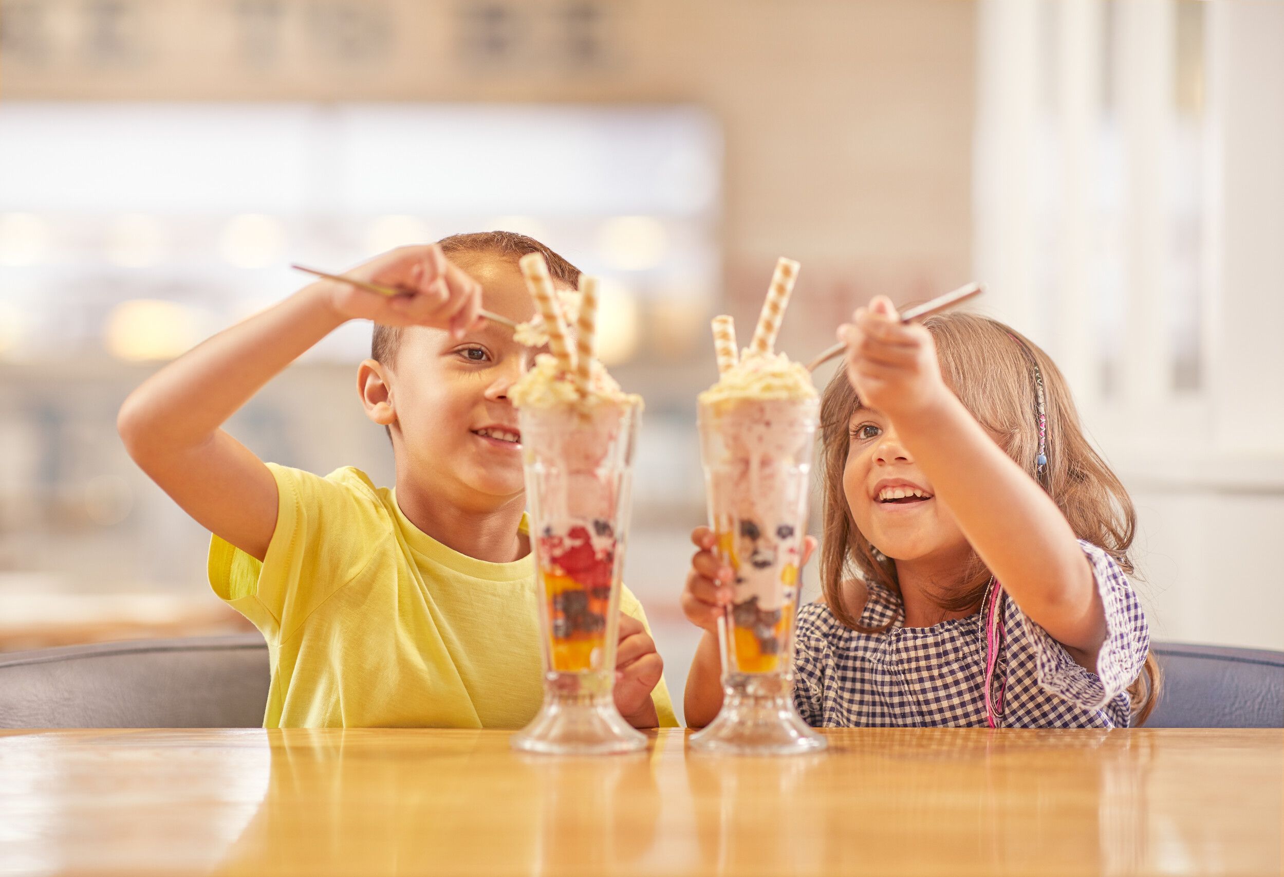 Two little kids enjoying their tall glasses of ice cream.