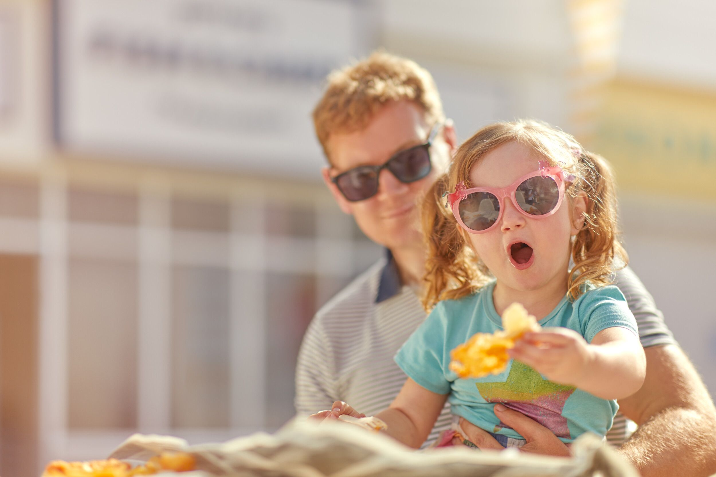 A father and his daughter sitting outdoors while having a snack.