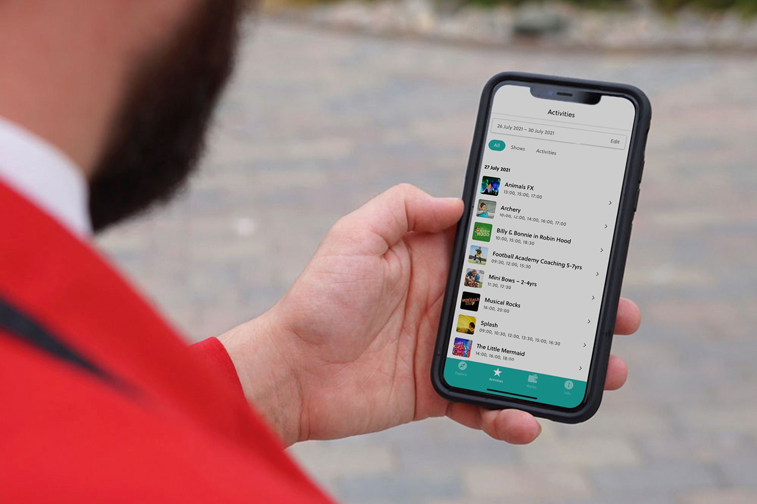 A Redcoat in their iconic red jacket, holding a smartphone displaying a schedule of activities on the Butlin’s app.