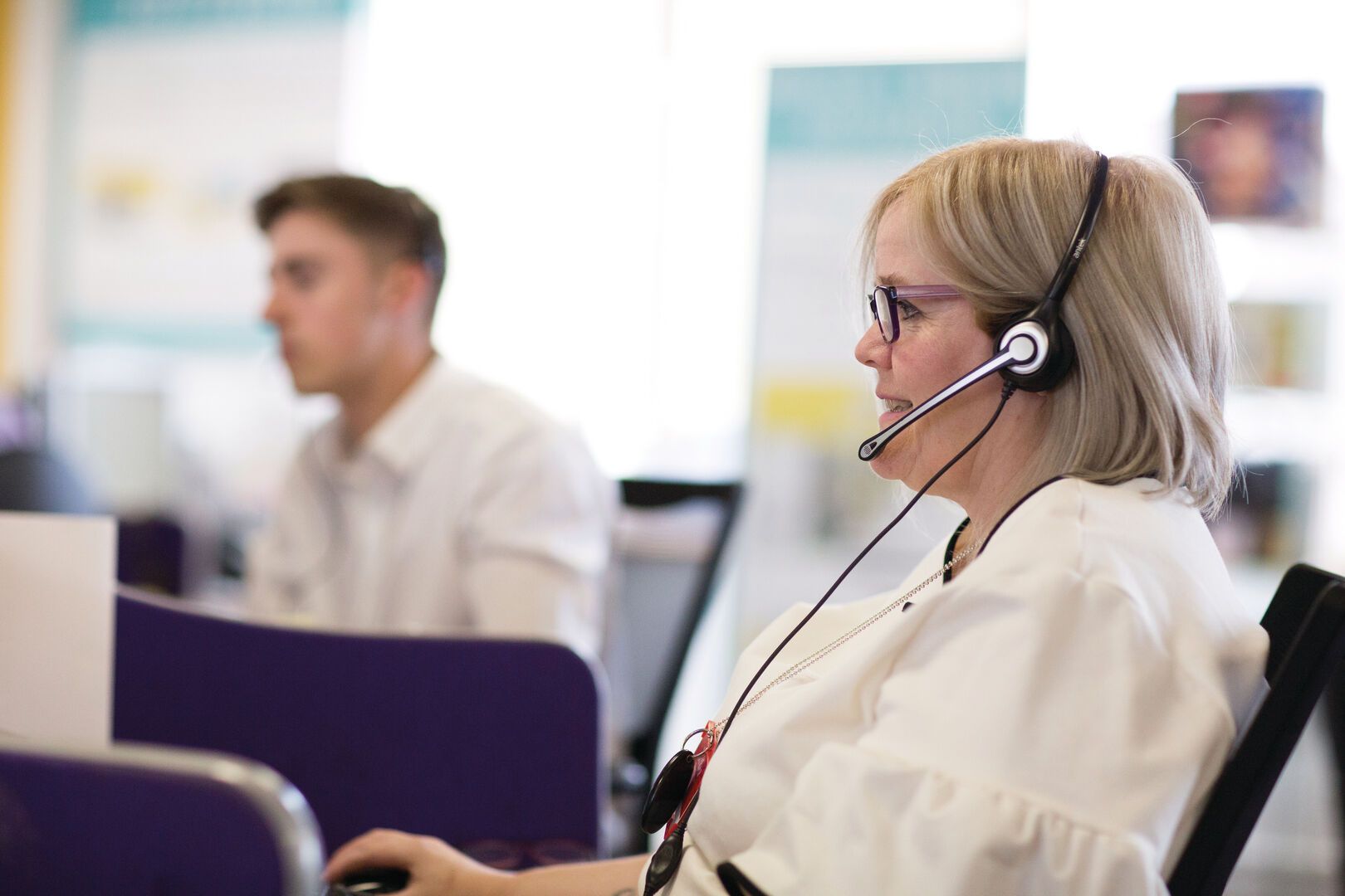 A photo of a team member at the Hemel Hempstead office. She wears a headset while working on her laptop.