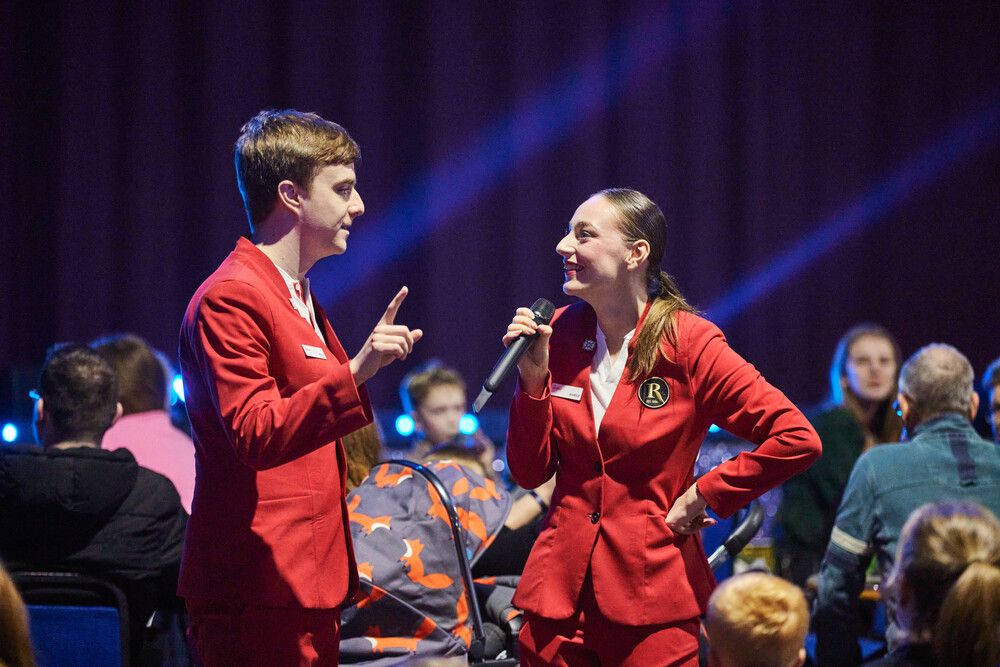 Two Butlin's Redcoats look at once another as they stand in amongst the audience during a live show.