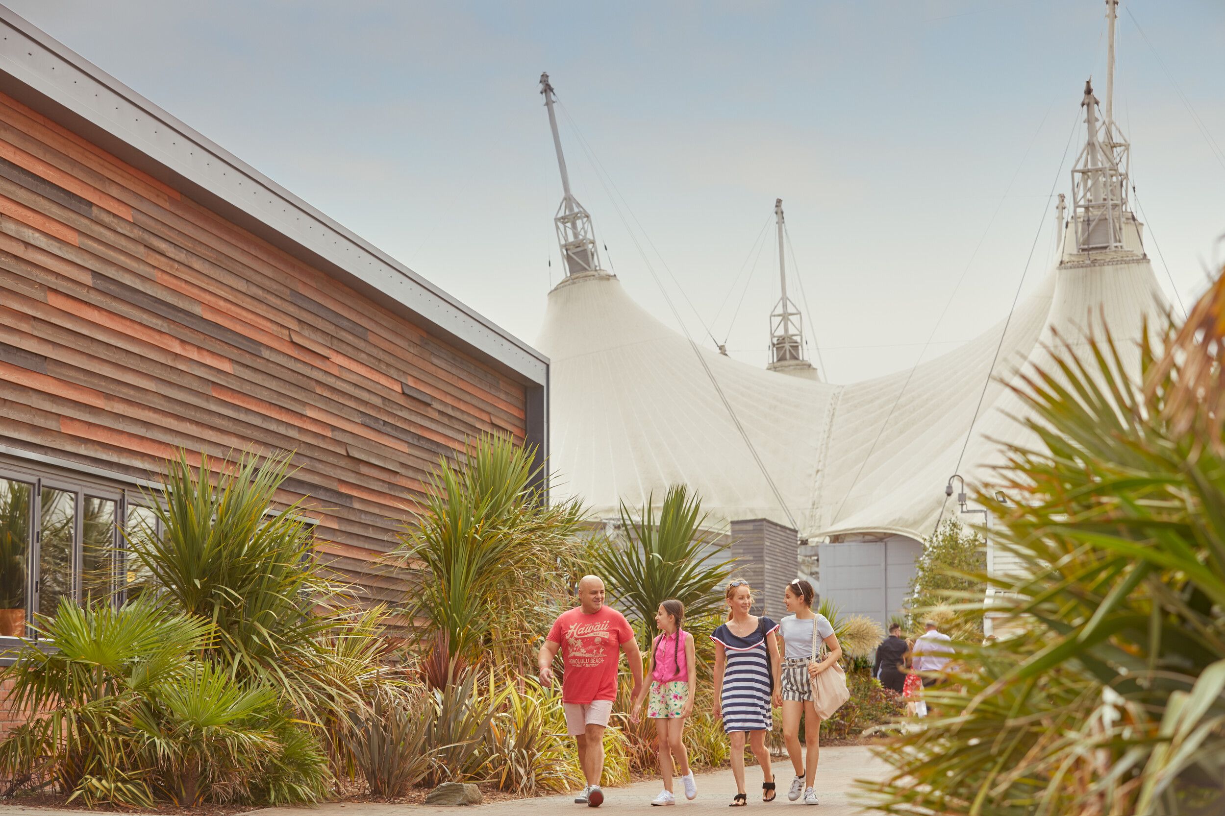 A photo of a family in front of the Skyline Pavilion at Butlin's Skegness, framed by palm trees on either side.