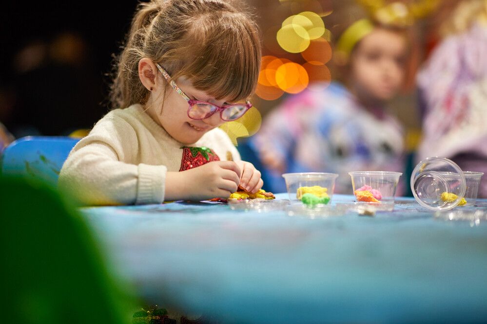 Young girl in glasses concentrates on decorating her Christmas craft at Butlin’s, with pots of bright materials spread out across the table.