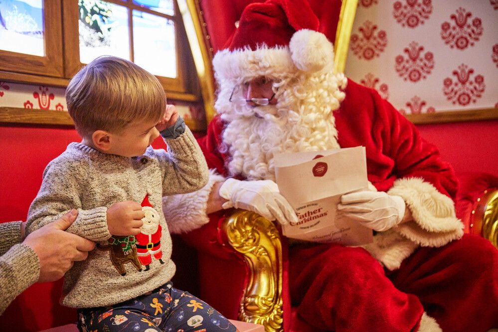 Father Christmas is holding a letter while talking to a young boy.