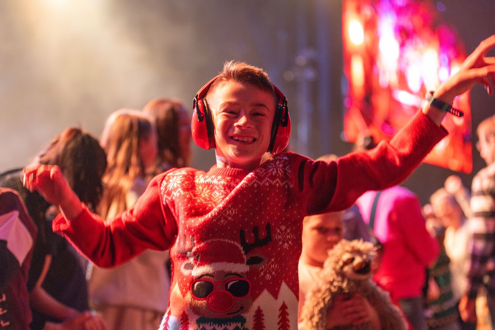 Happy boy in red Christmas jumper and ear defenders dancing at a Butlin’s family Christmas break show.