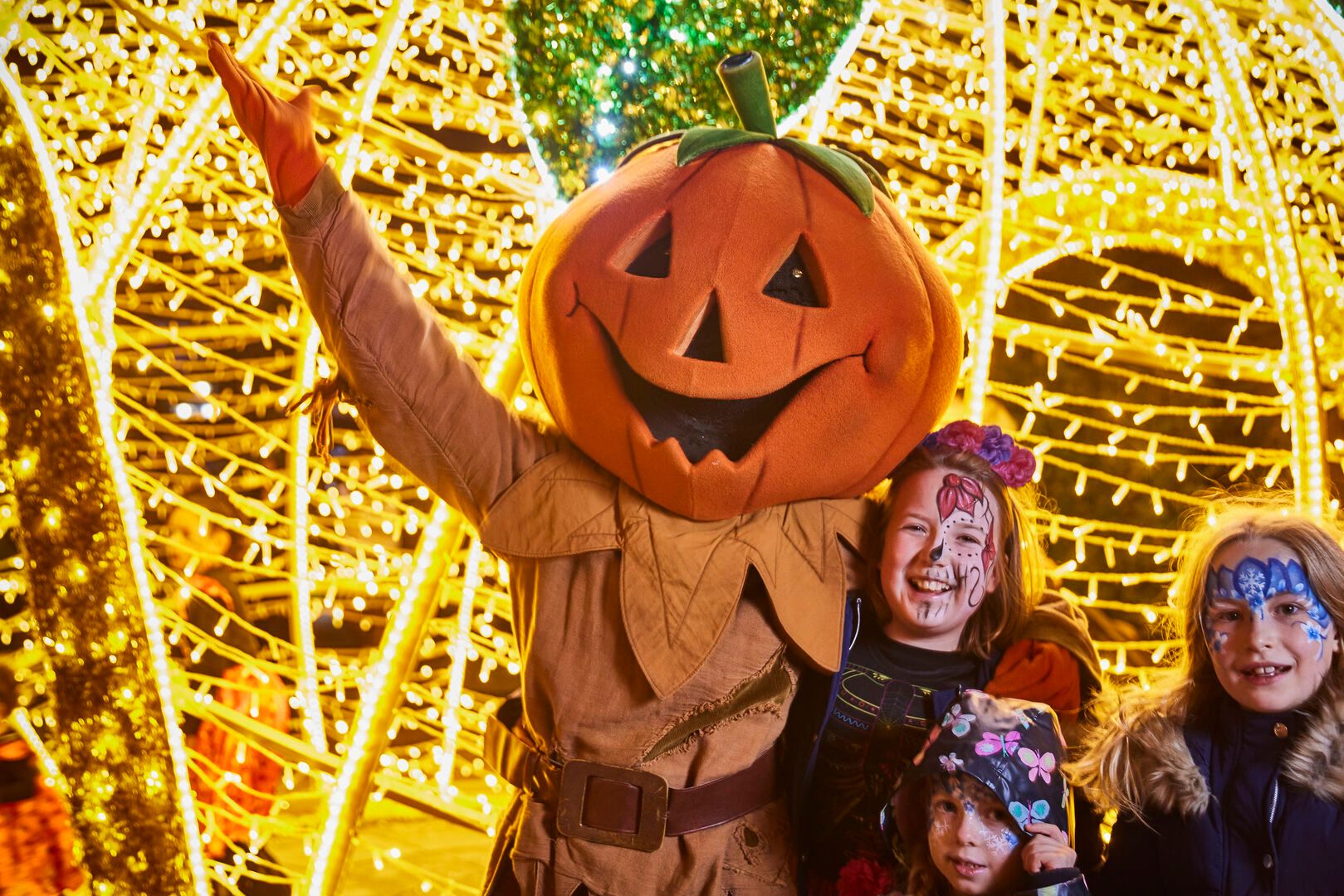 Three young children pose for a photo with a pumpkin mascot.