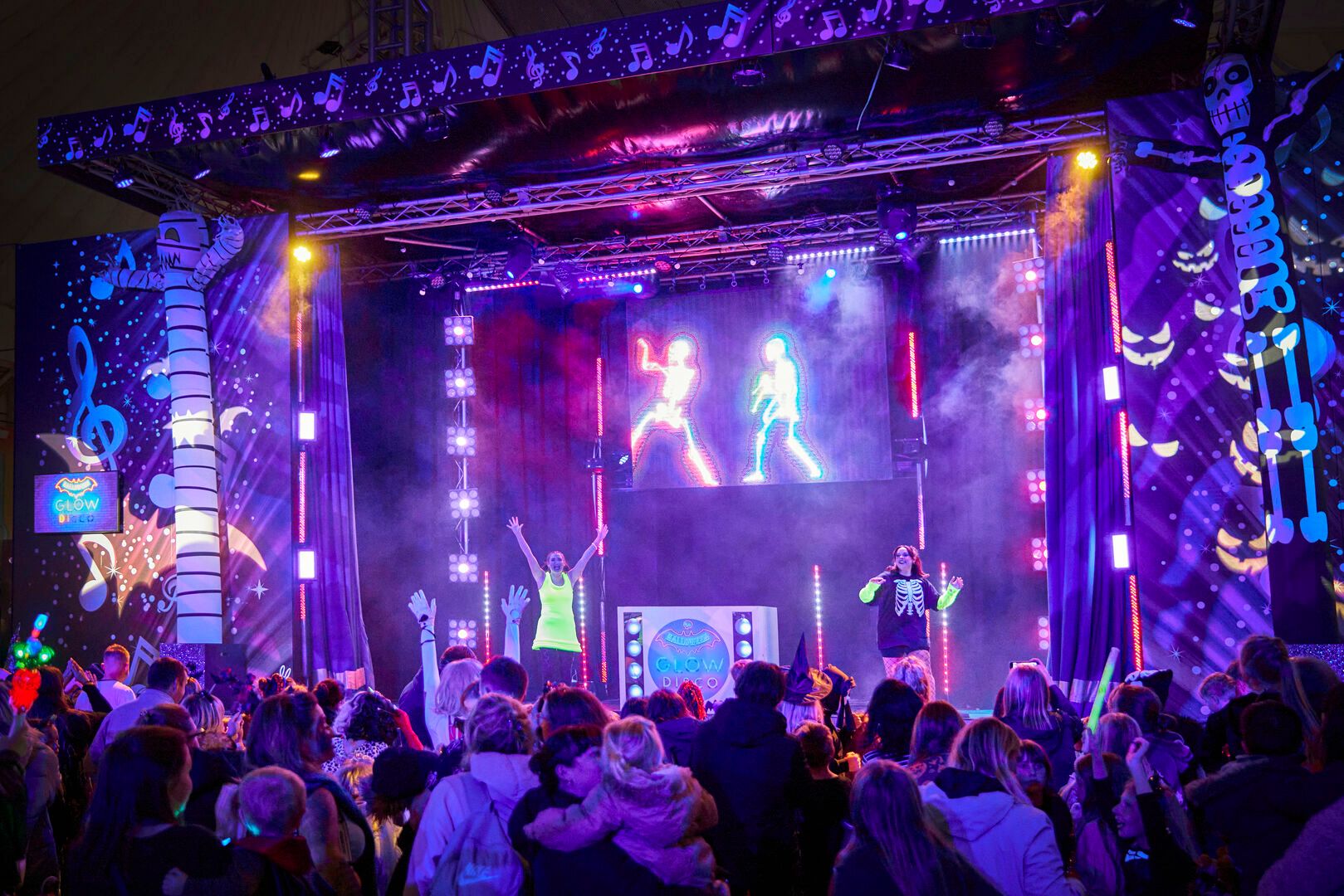 Two performers in spooky outfits perform to a large family audience.
