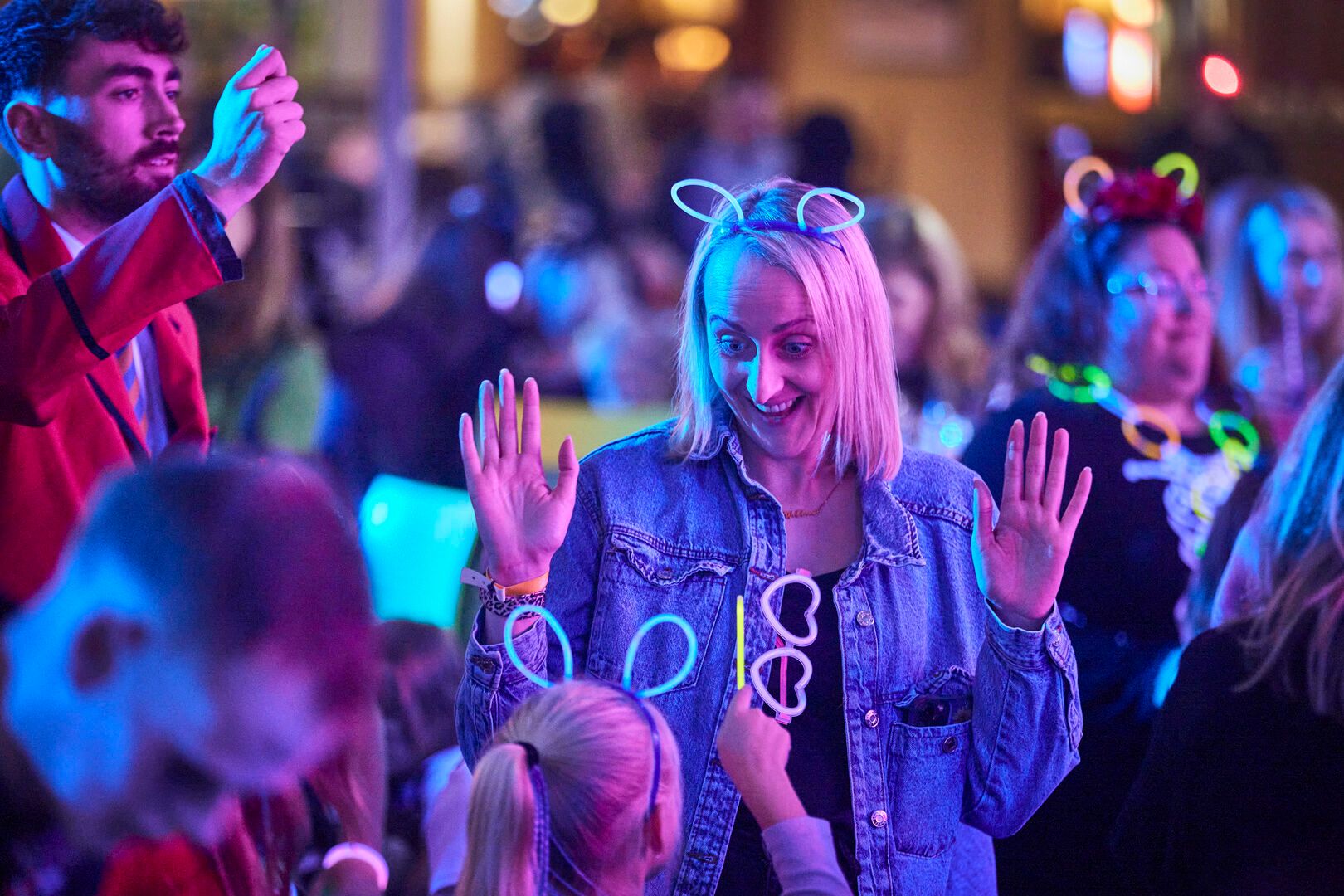 The crowd during Halloween Glow Disco at Butlin's. A Mum and her child play together with neon headbands and glasses.