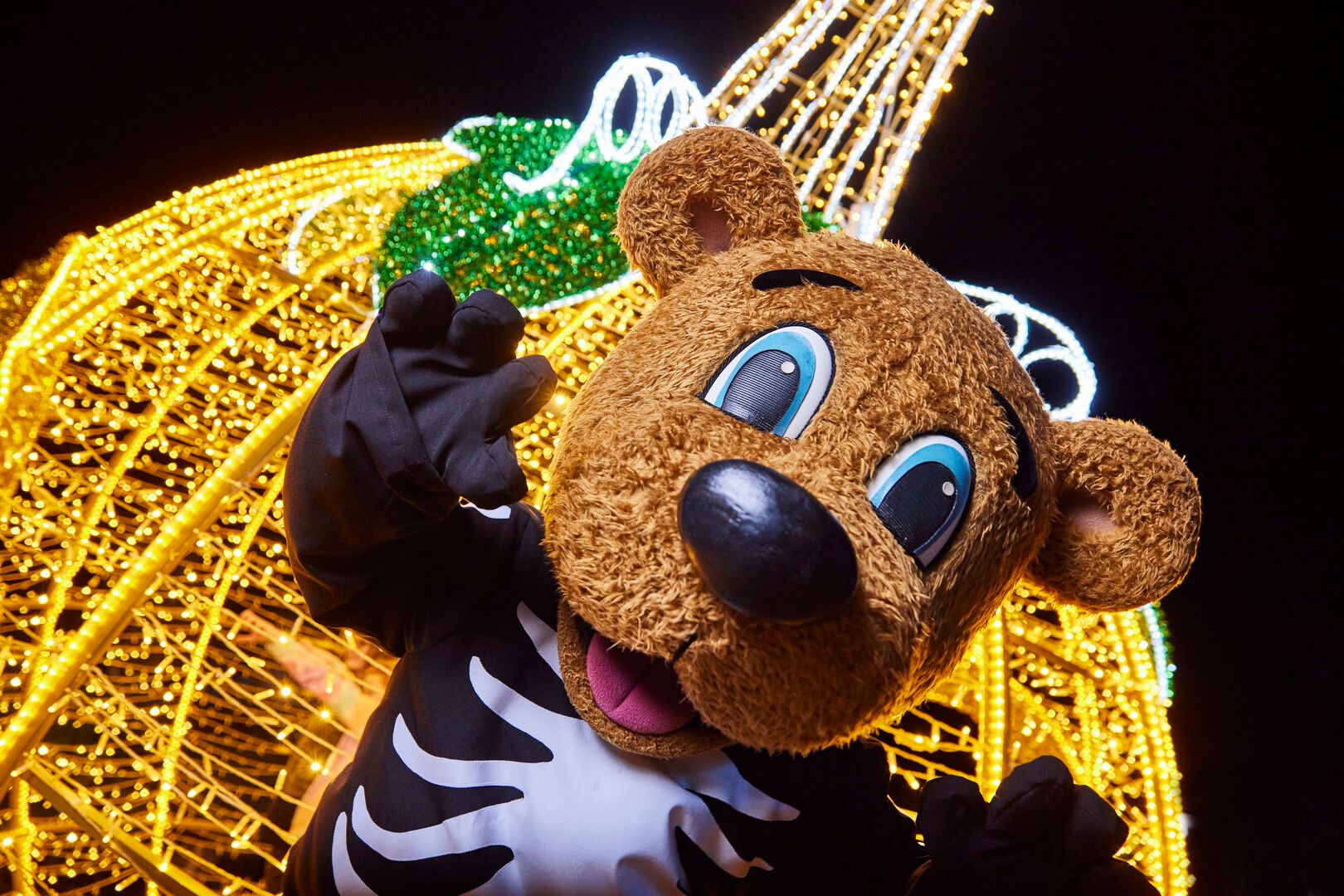 Billy Bear dressed in a skeleton costume for Halloween, poses in front of a large, lit-up pumpkin decoration.