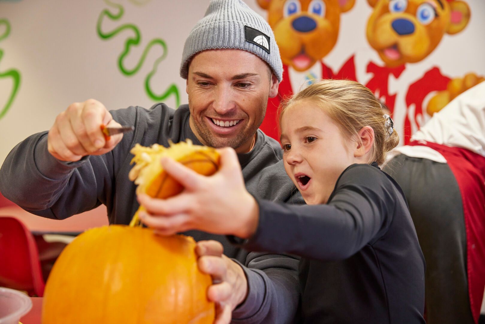 A father and daughter scoop out the inside of a pumpkin and have fun during the pumpkin carving activity.