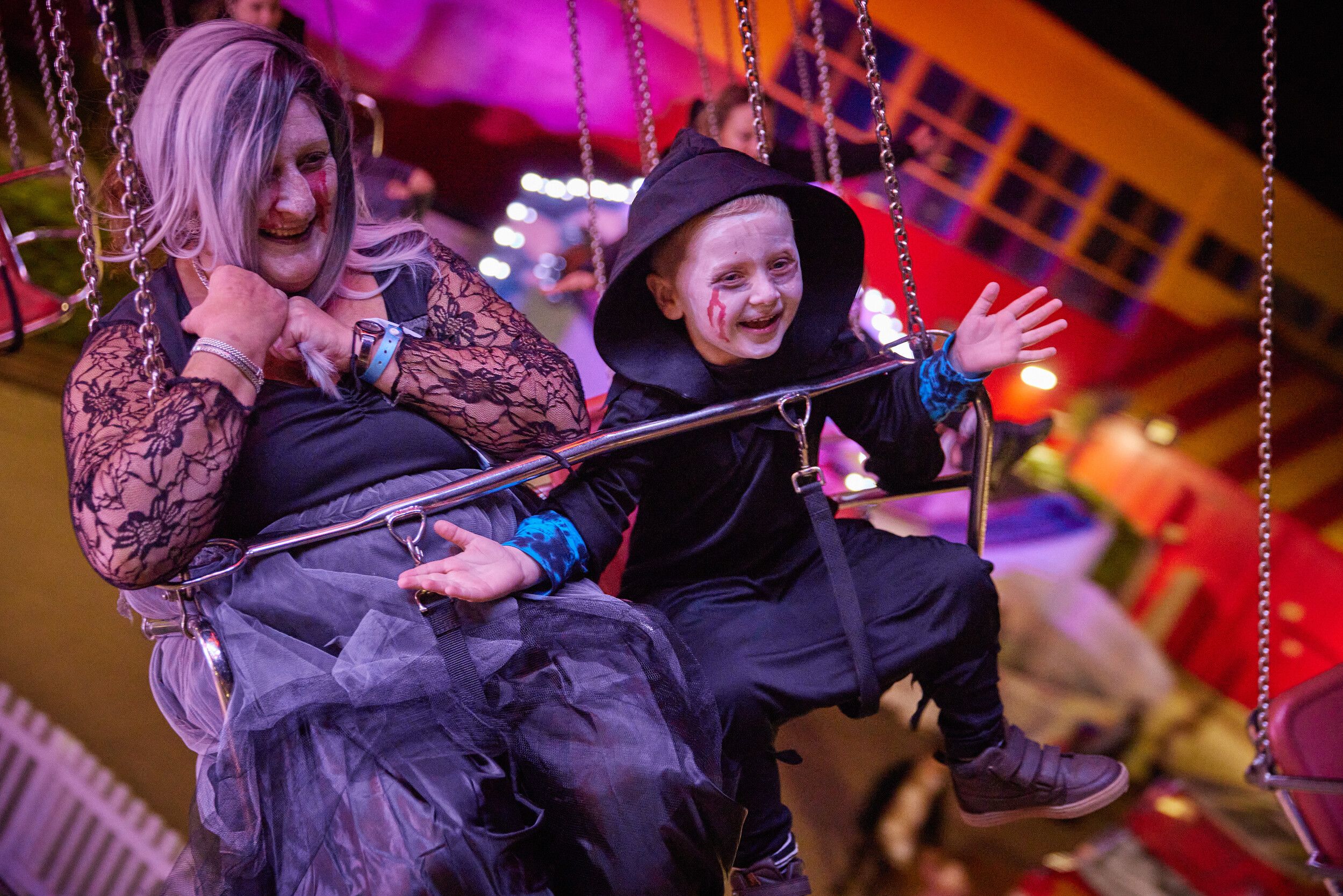 A mother and a child both with face paint riding a swing at the fairground.