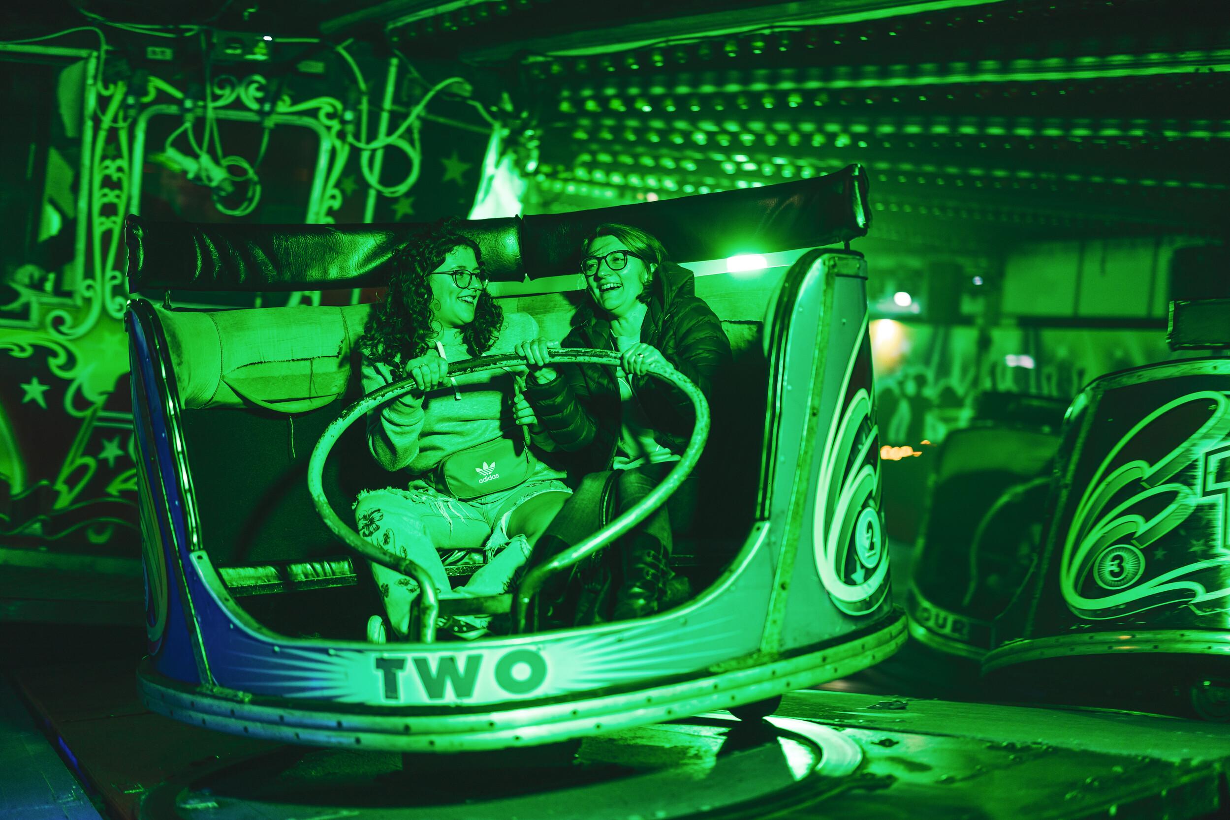 A photo of two guests on the Waltzer fairground ride, which has spooky green lighting for Halloween.