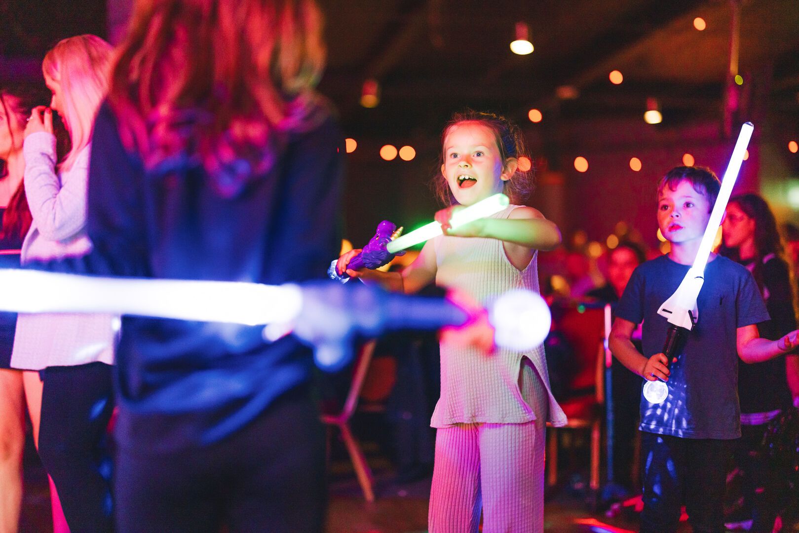 Four young children play with lightsabers.