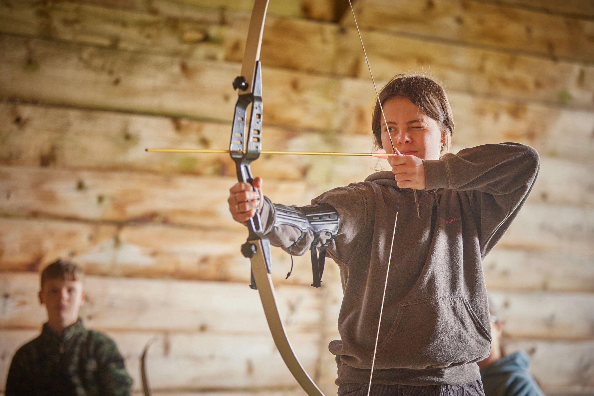 A girl aiming at a target with a bow and arrow.