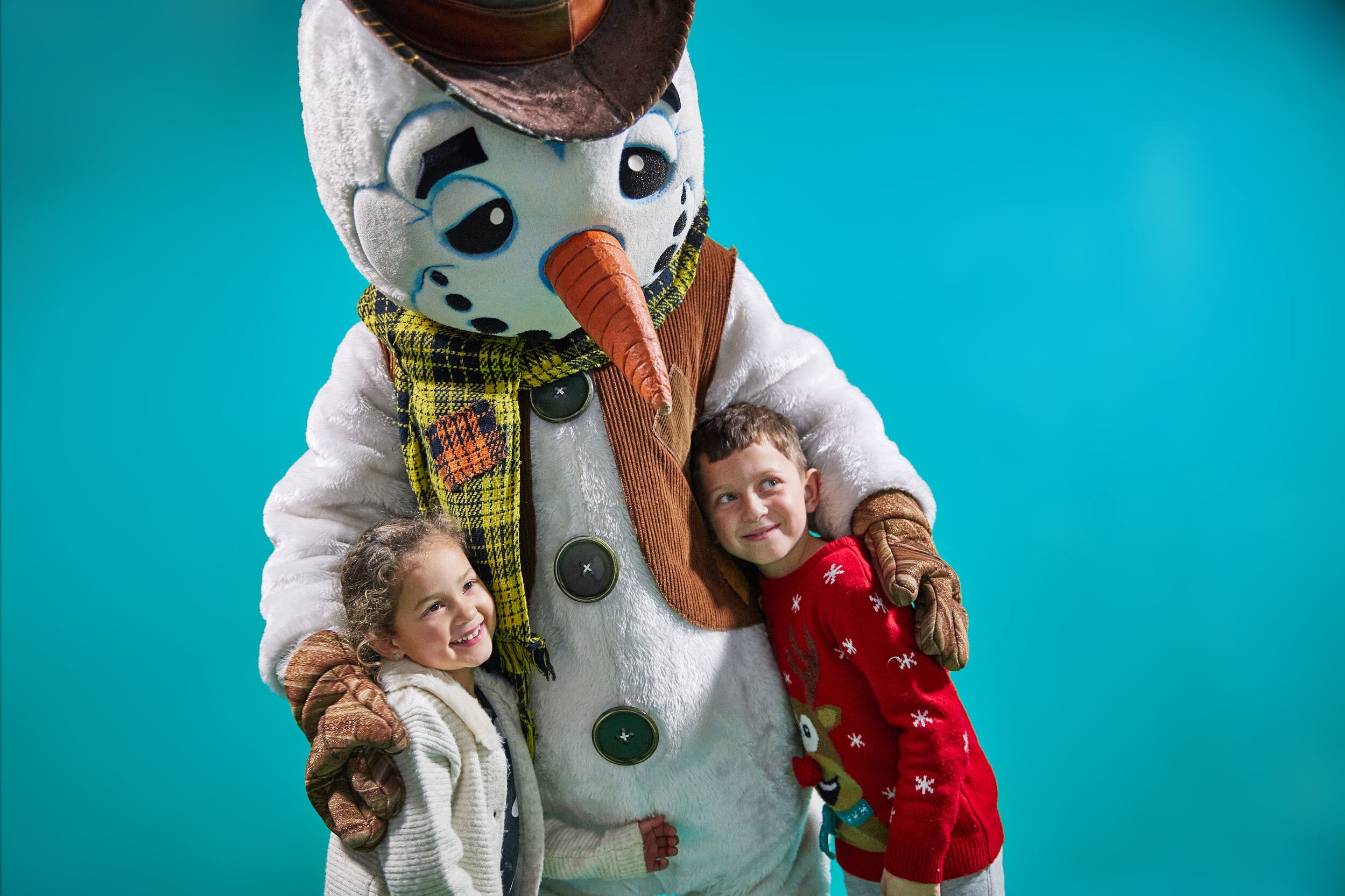 Two children and a snowman mascot posing at the camera.