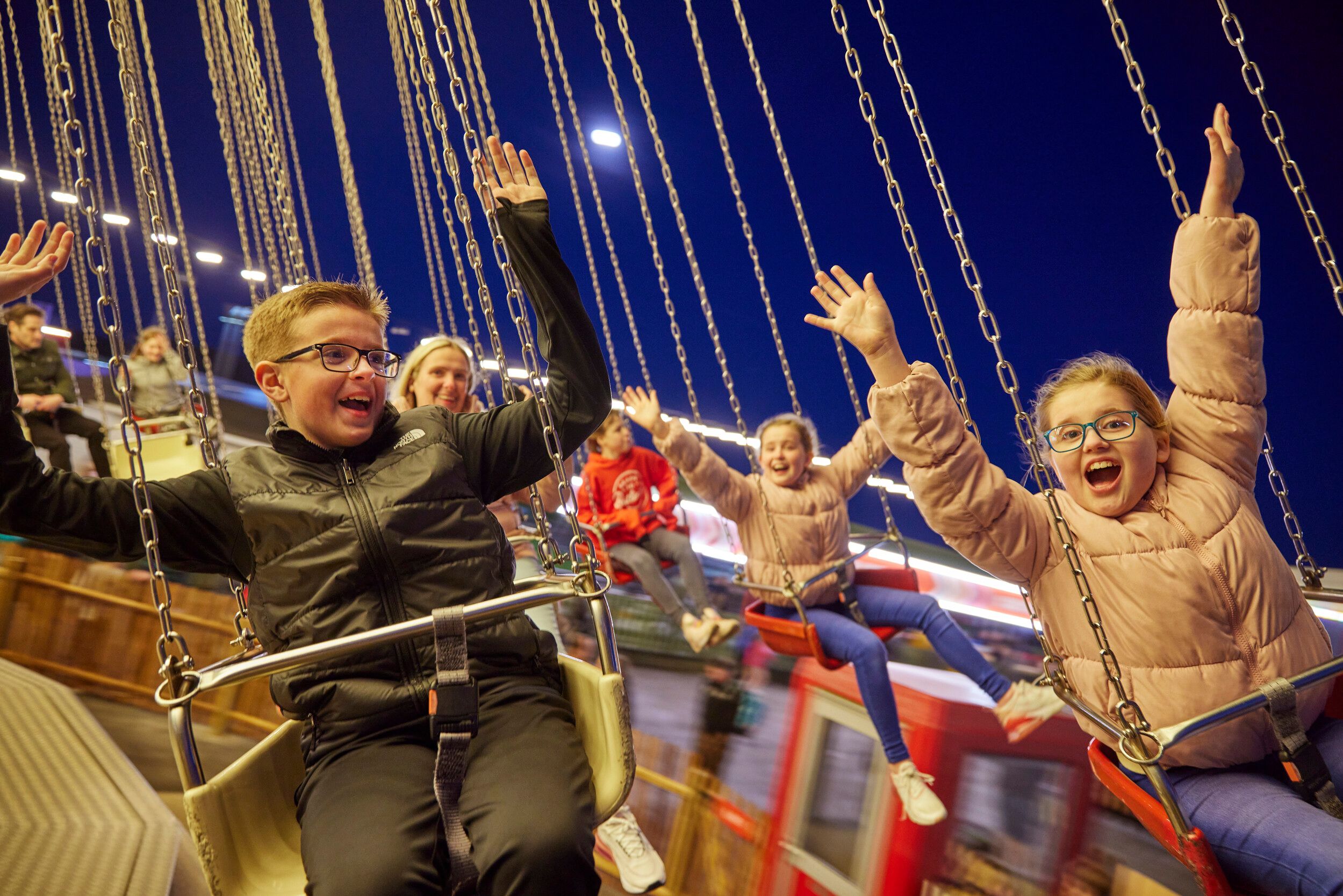 A close up of children having fun with their hands in the air, while riding the Chairoplane fairground ride.