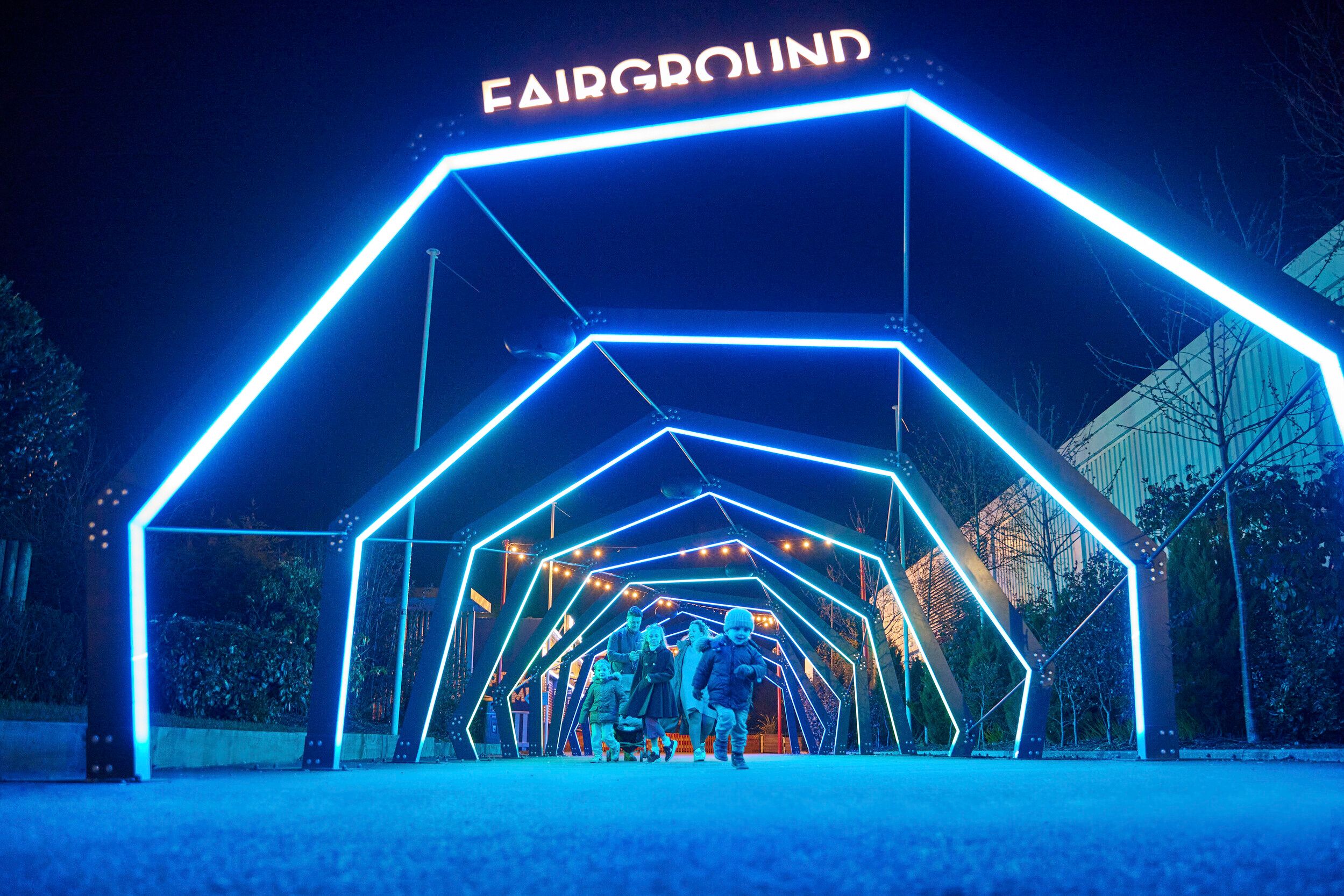 A family walk under several neon archways that lead to the Skegness fairground.