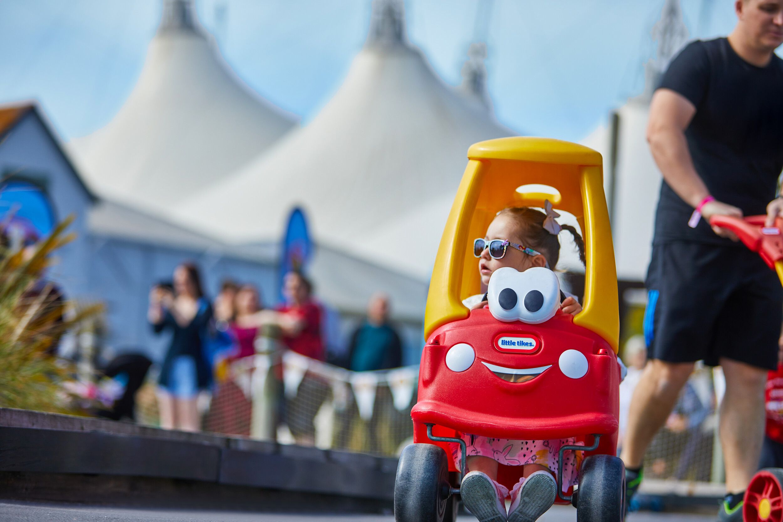 A little girl wearing glasses while riding a toy car outdoors.