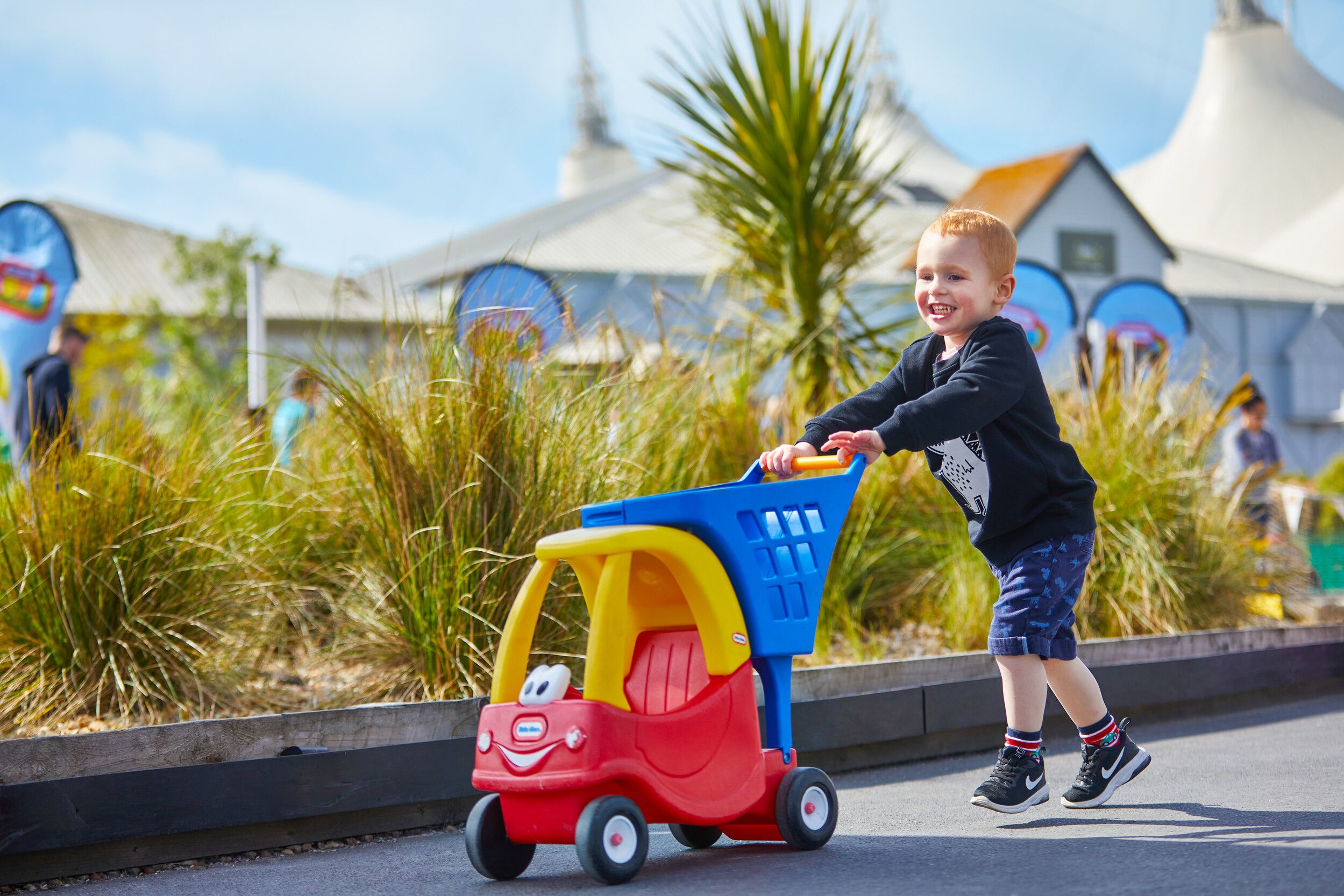 A boy happily pushing a toy car outdoors.