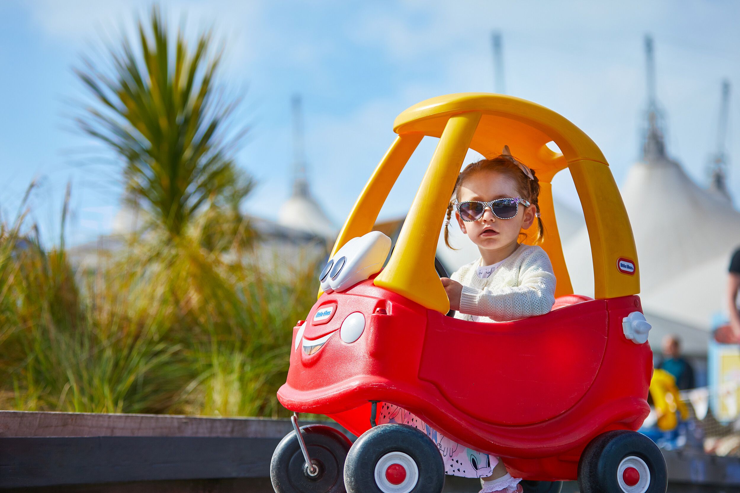 A little girl wearing glasses while riding a toy car.