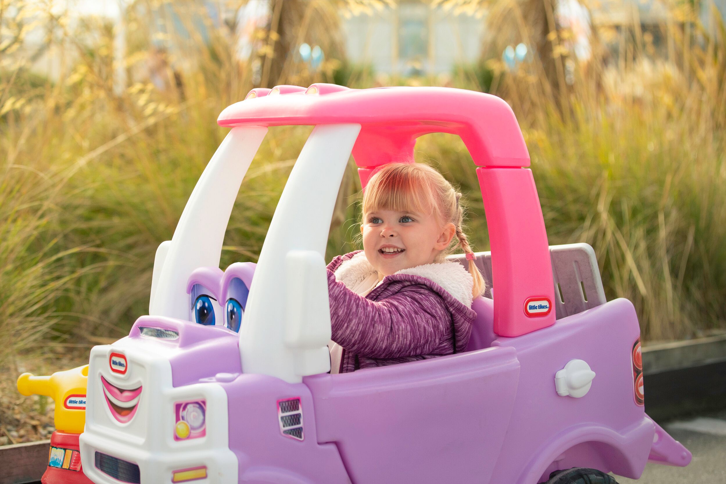A little girl smiling while riding a toy car.