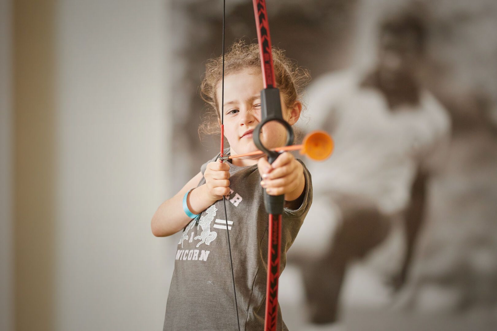 A close-up of a young girl holding and aiming a mini-bow.