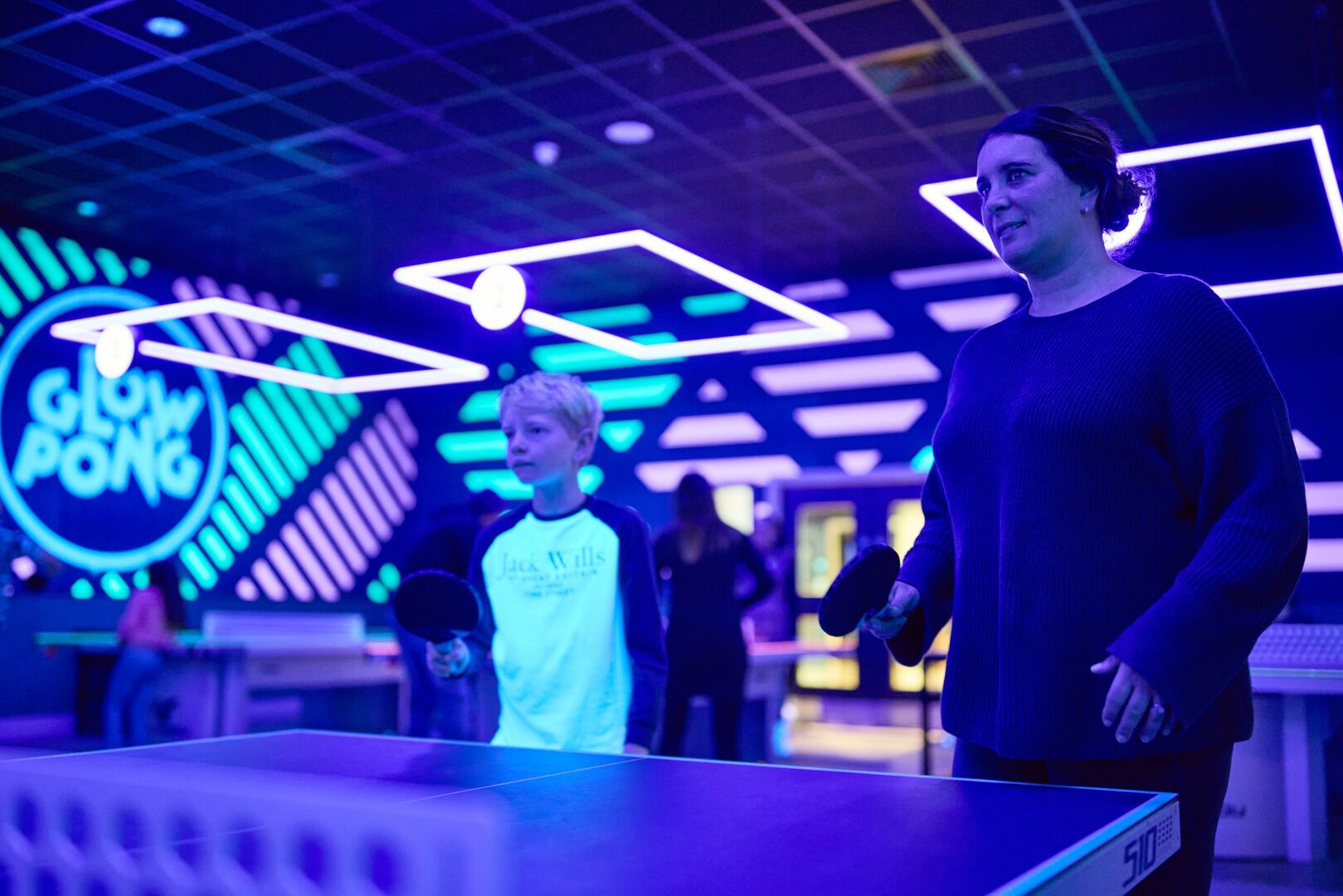 A mother and son play Glow Pong together.