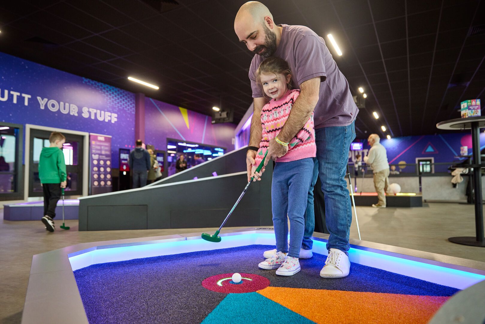 A father teaches his daughter to play golf.