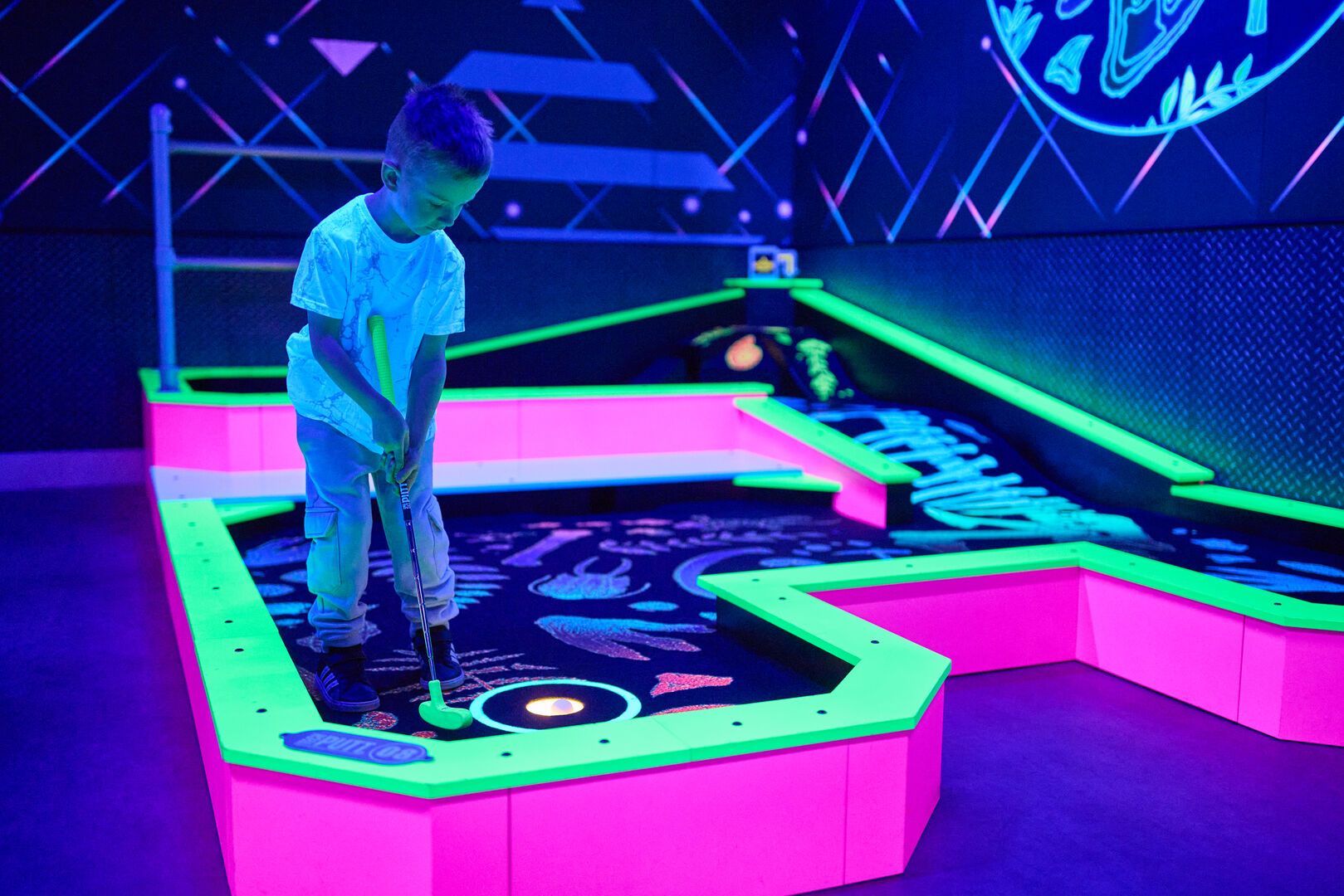 A young boy hits the golf ball into the cup while playing Tech Putt.