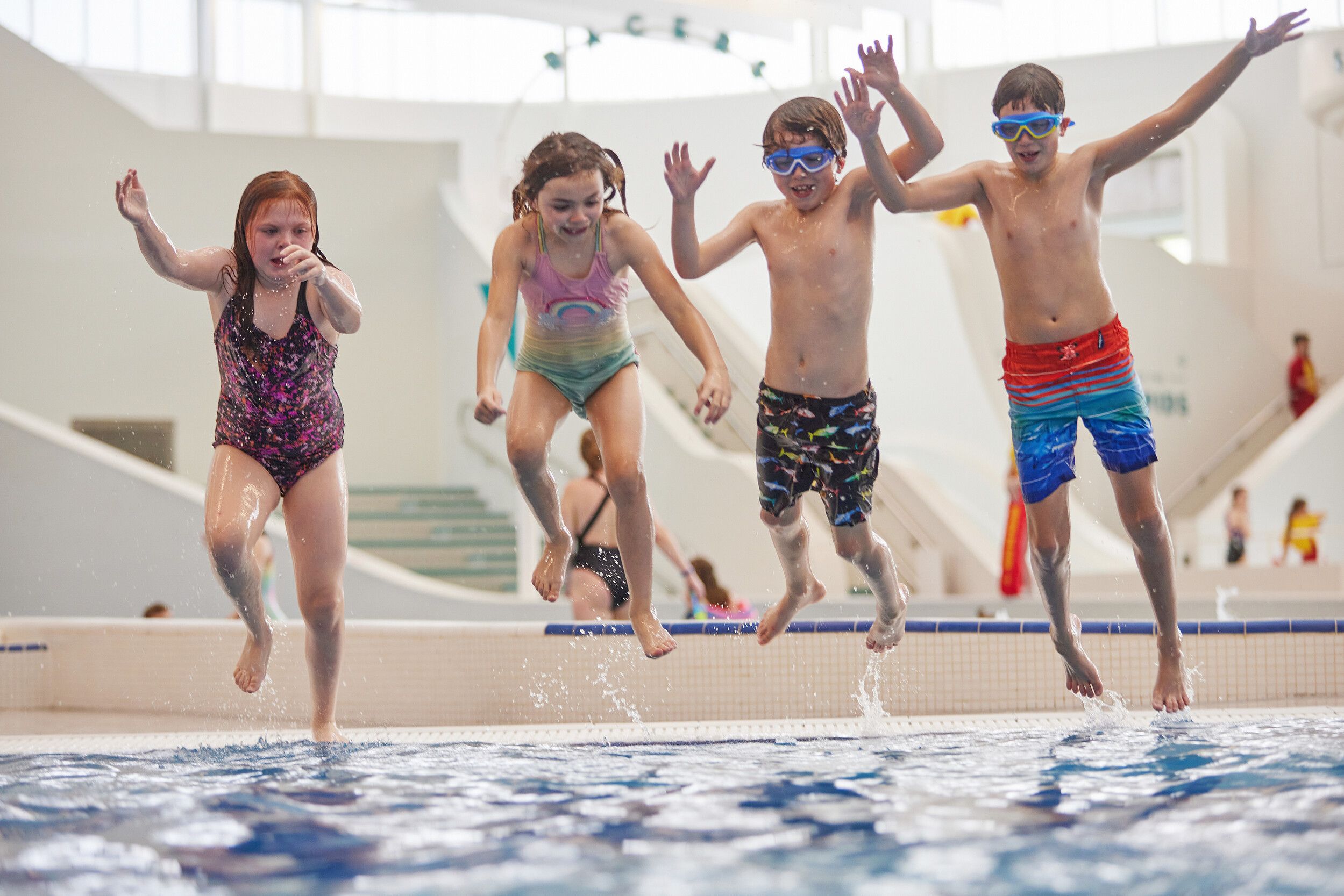 Four kids jumping in to the pool at the same time.