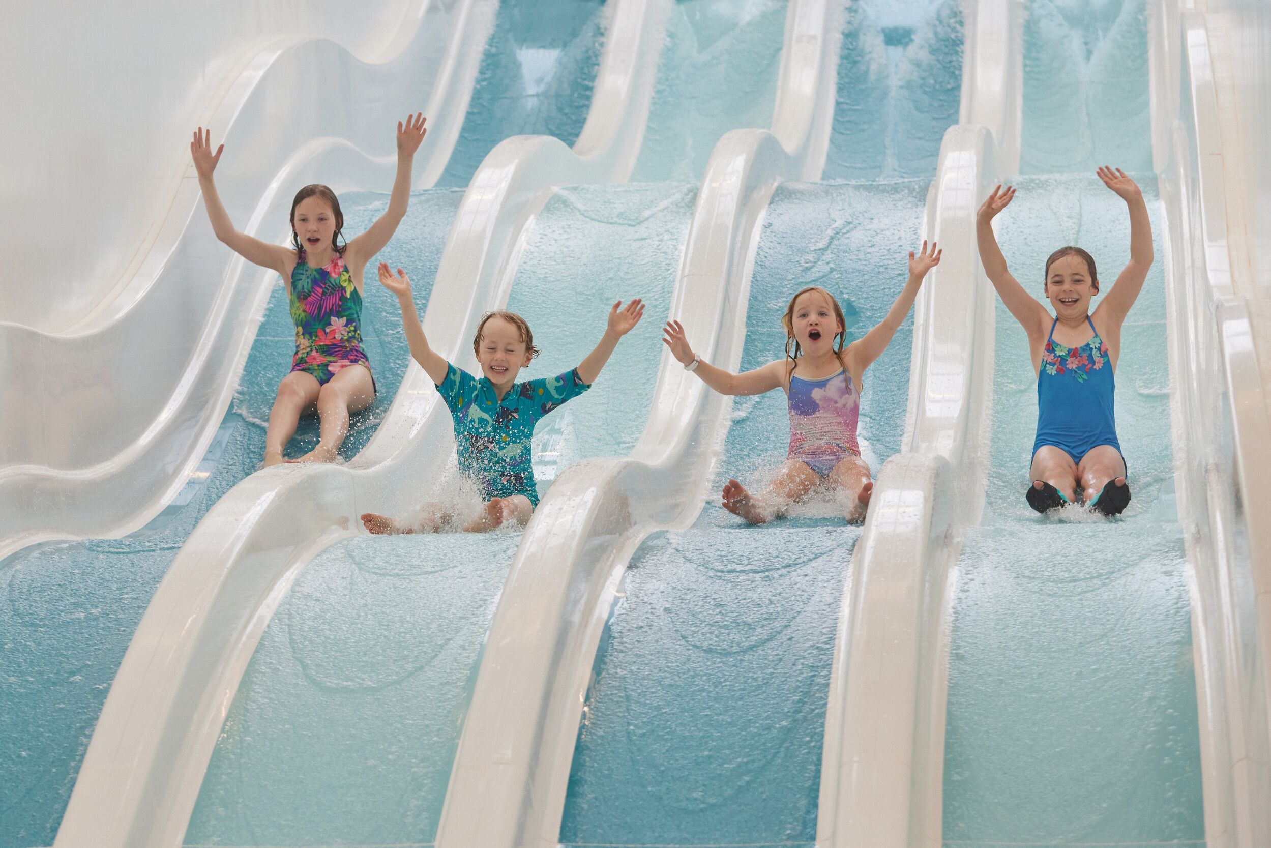 Four kids raising their hands while going down a blue water slide at the same time